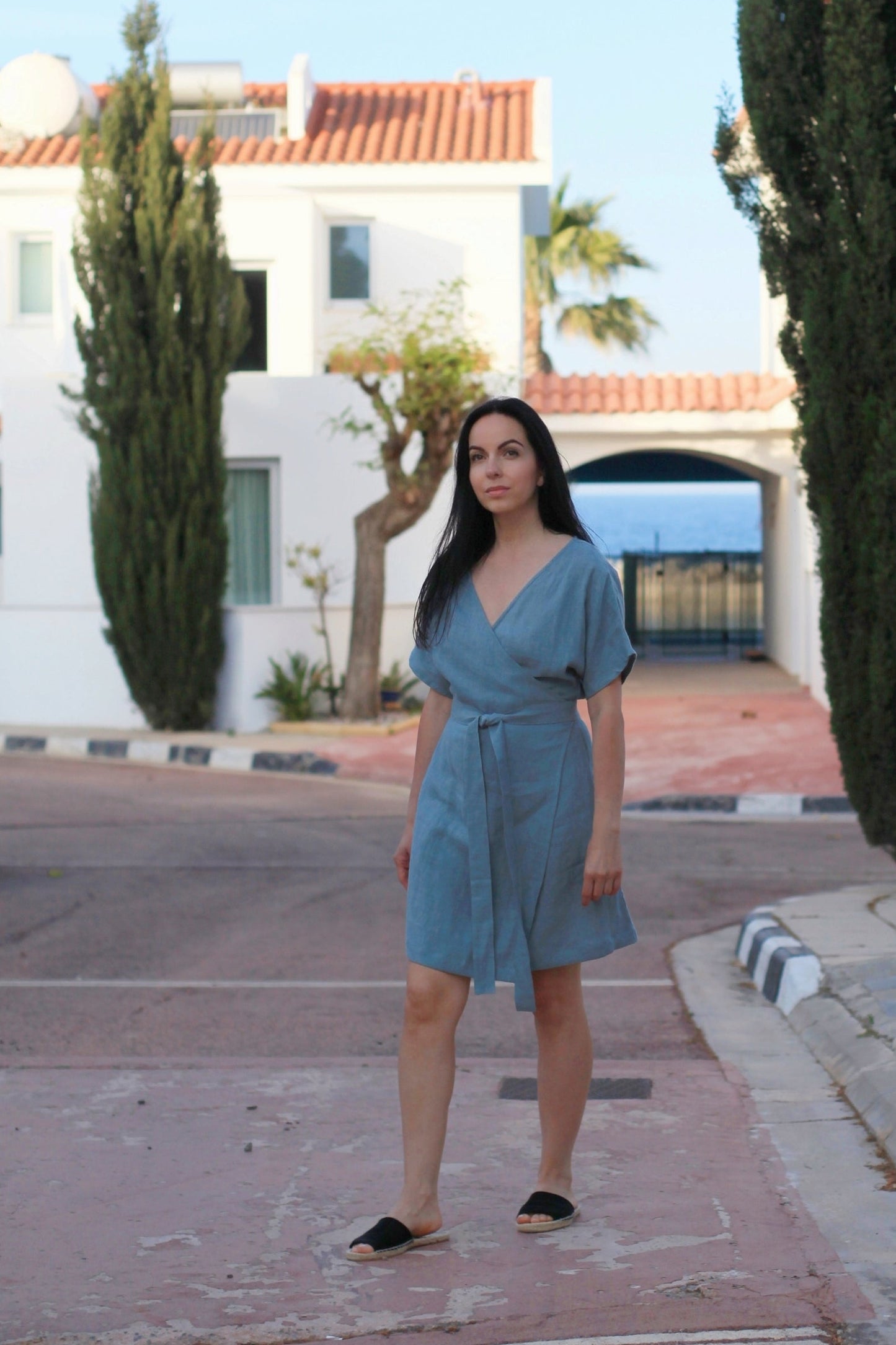 Woman in a blue dress standing on a street with white houses and greenery in the background