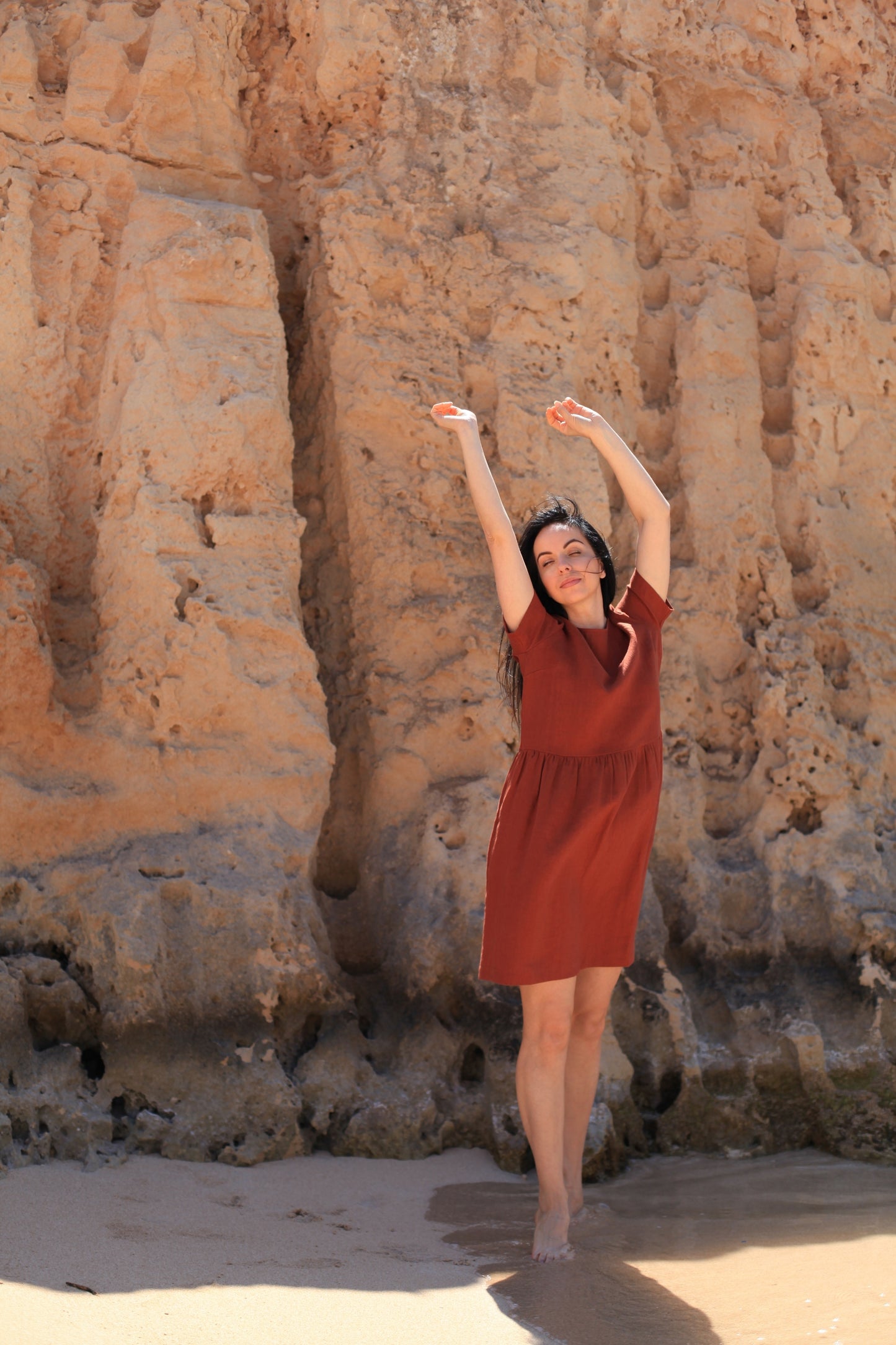 Woman in a red dress standing against a rocky cliff.