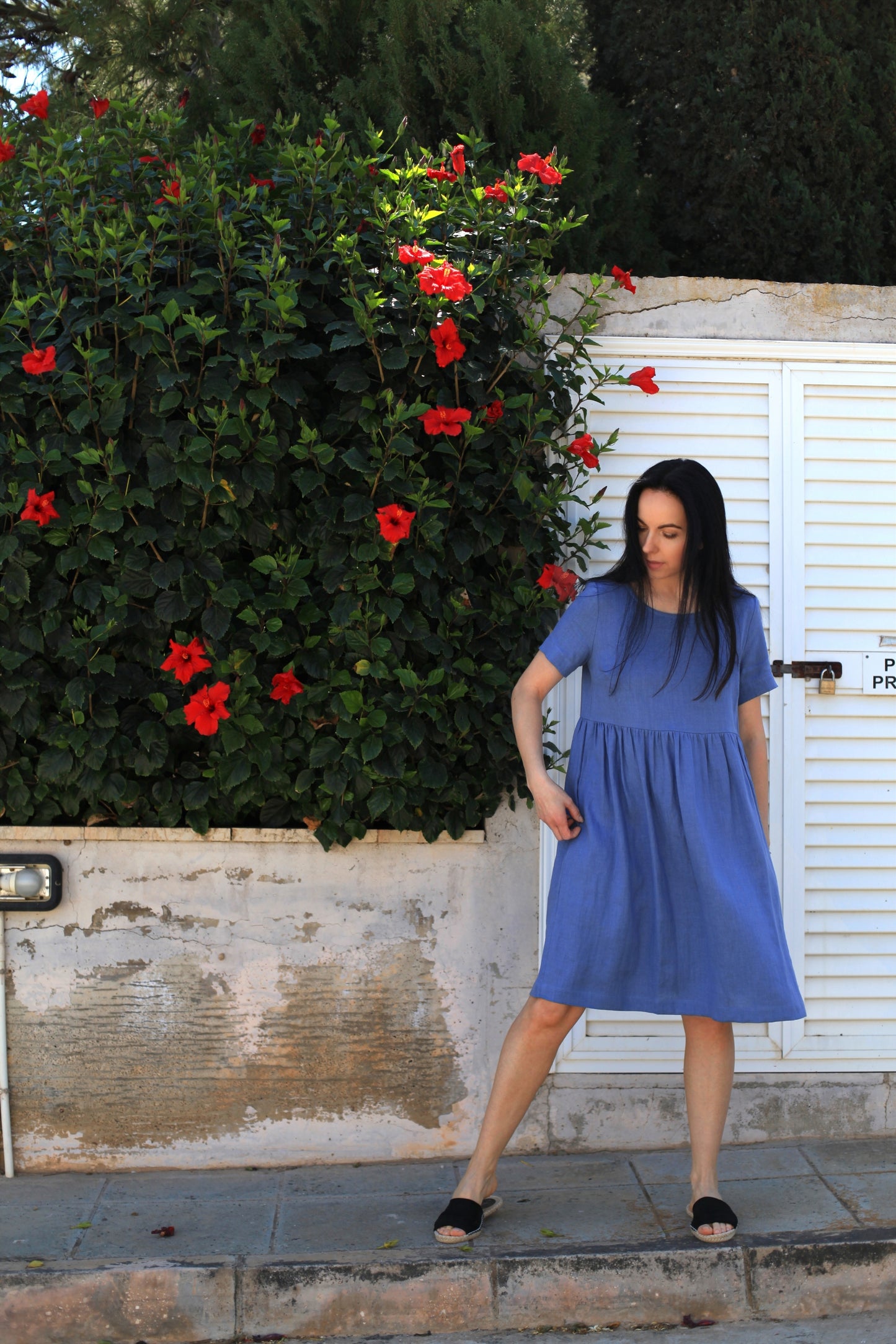 Woman in a blue dress standing in front of a white wall with red flowers.