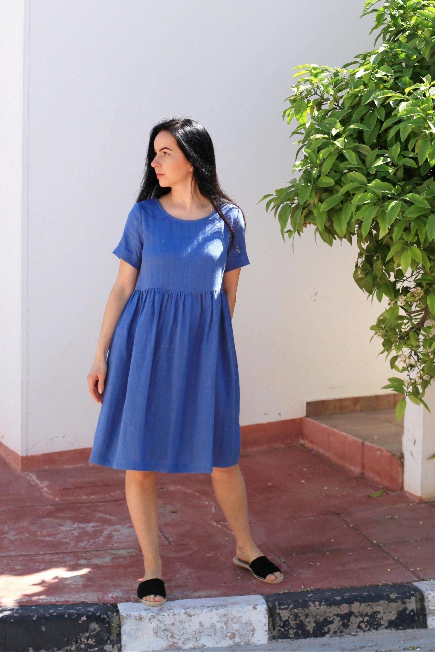 Woman in a blue dress standing outdoors next to a building and tree