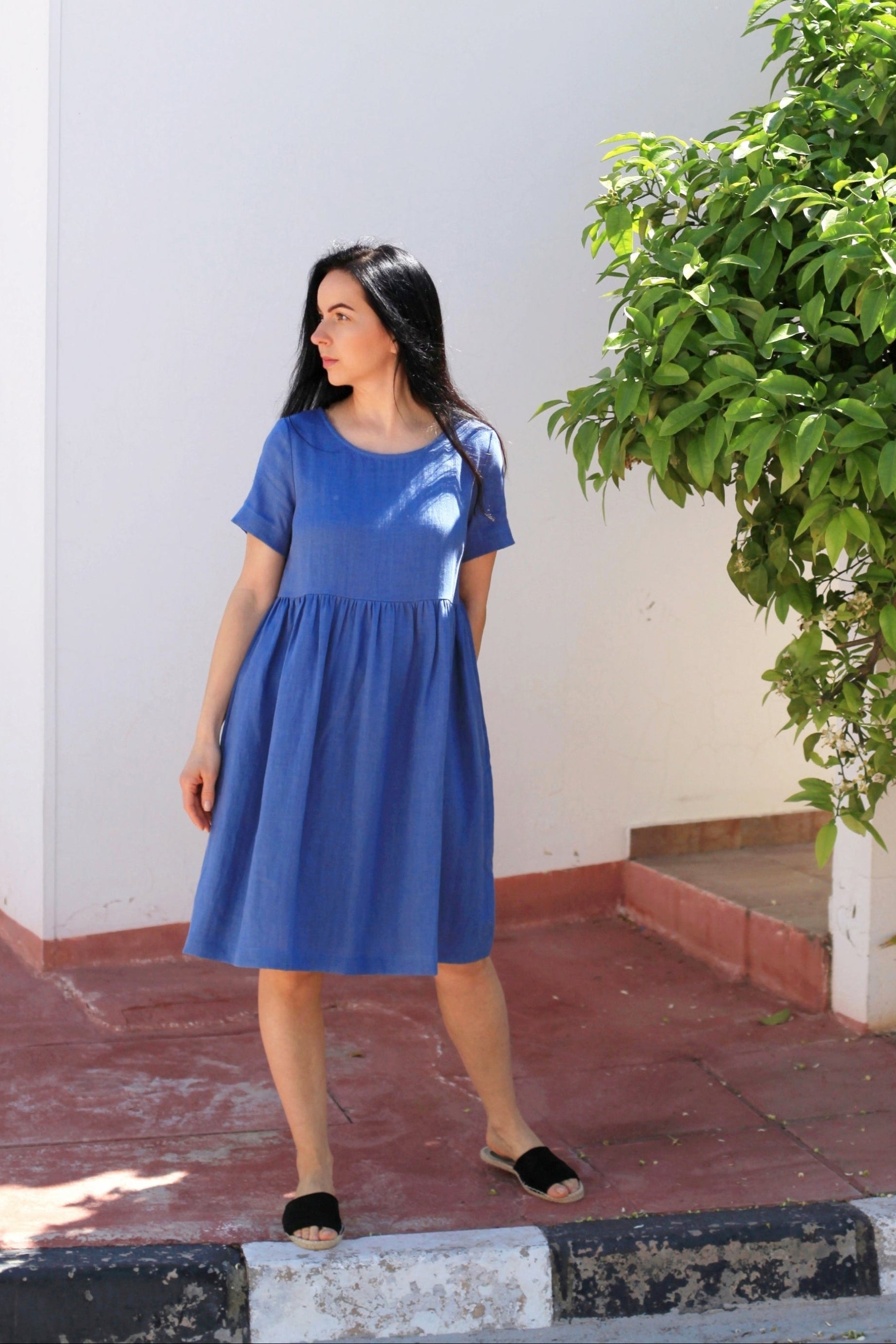 Woman in a blue dress standing outdoors next to a building and tree