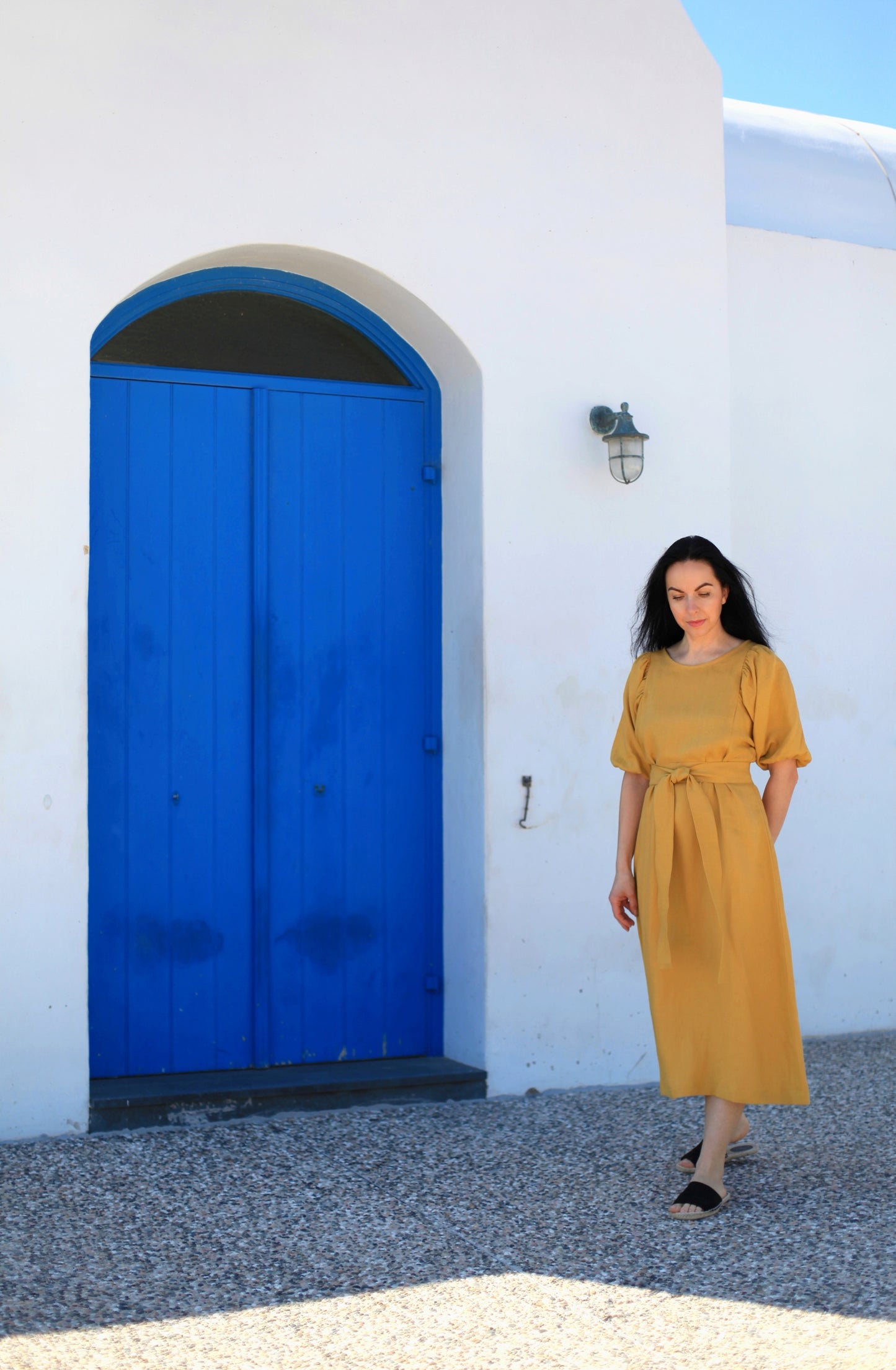 Woman in a yellow dress standing in front of a blue door and white wall.