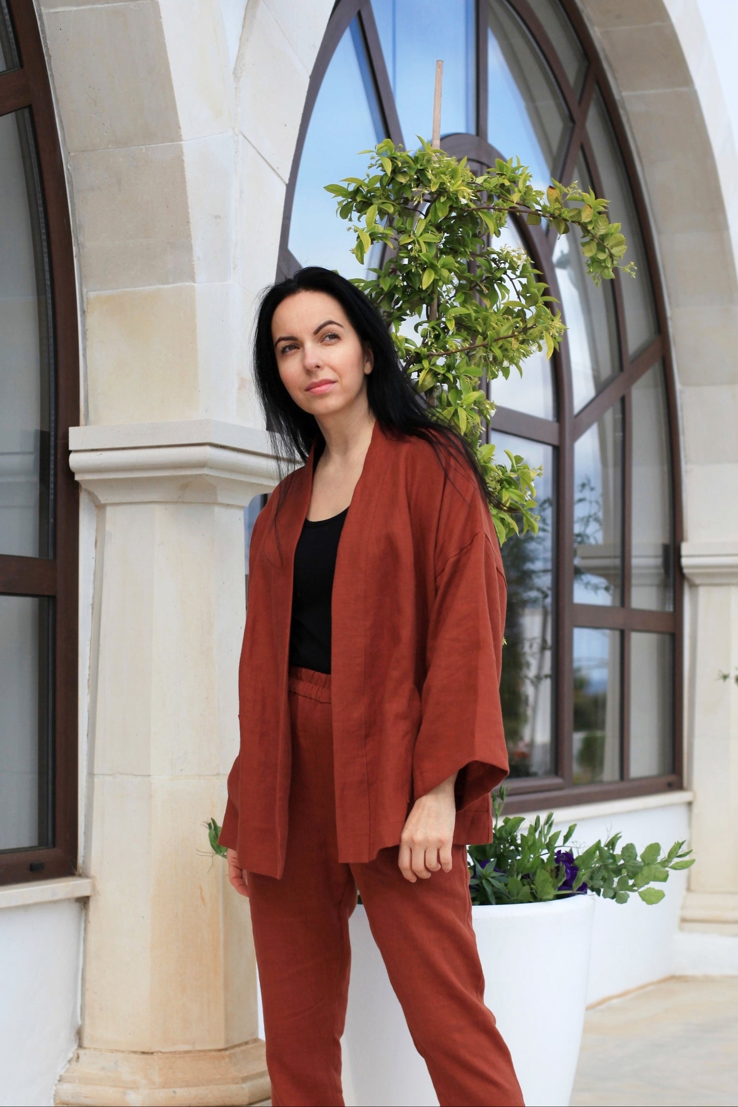 Woman in a red outfit standing in front of a building with large windows and plants.