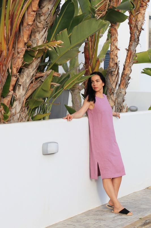Woman in a pink dress standing against a white wall with palm trees in the background