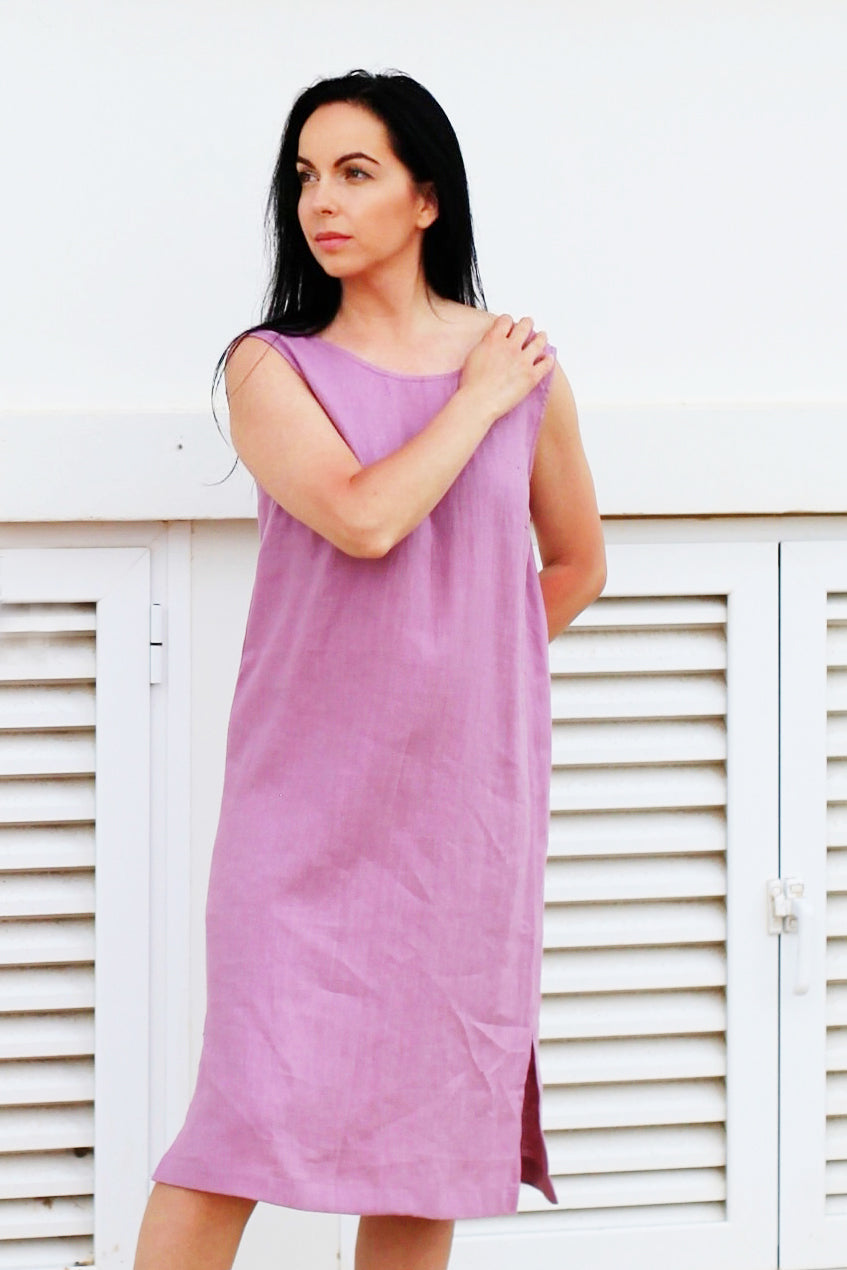 Woman wearing a pink dress standing against a white wooden background