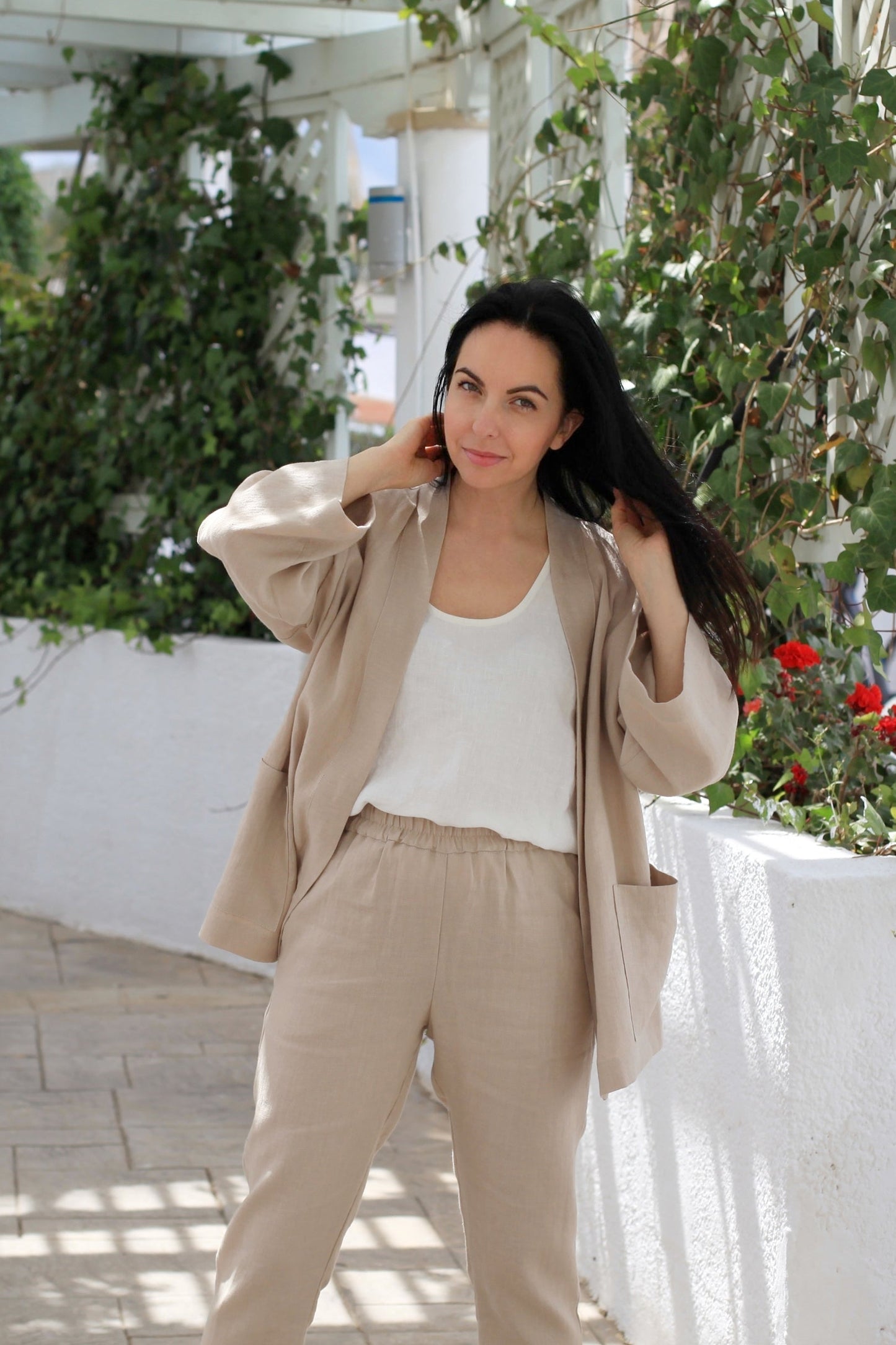 Woman in beige outfit standing in a garden with white columns and greenery