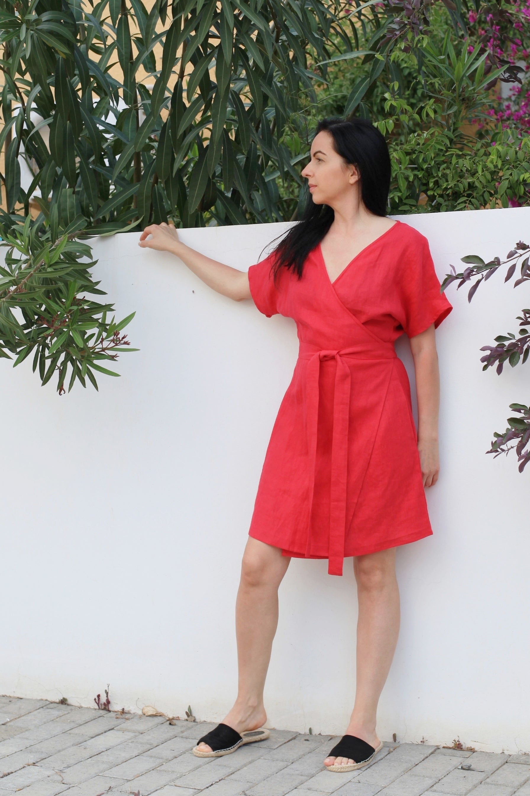 Woman in a red dress standing against a white wall with greenery around