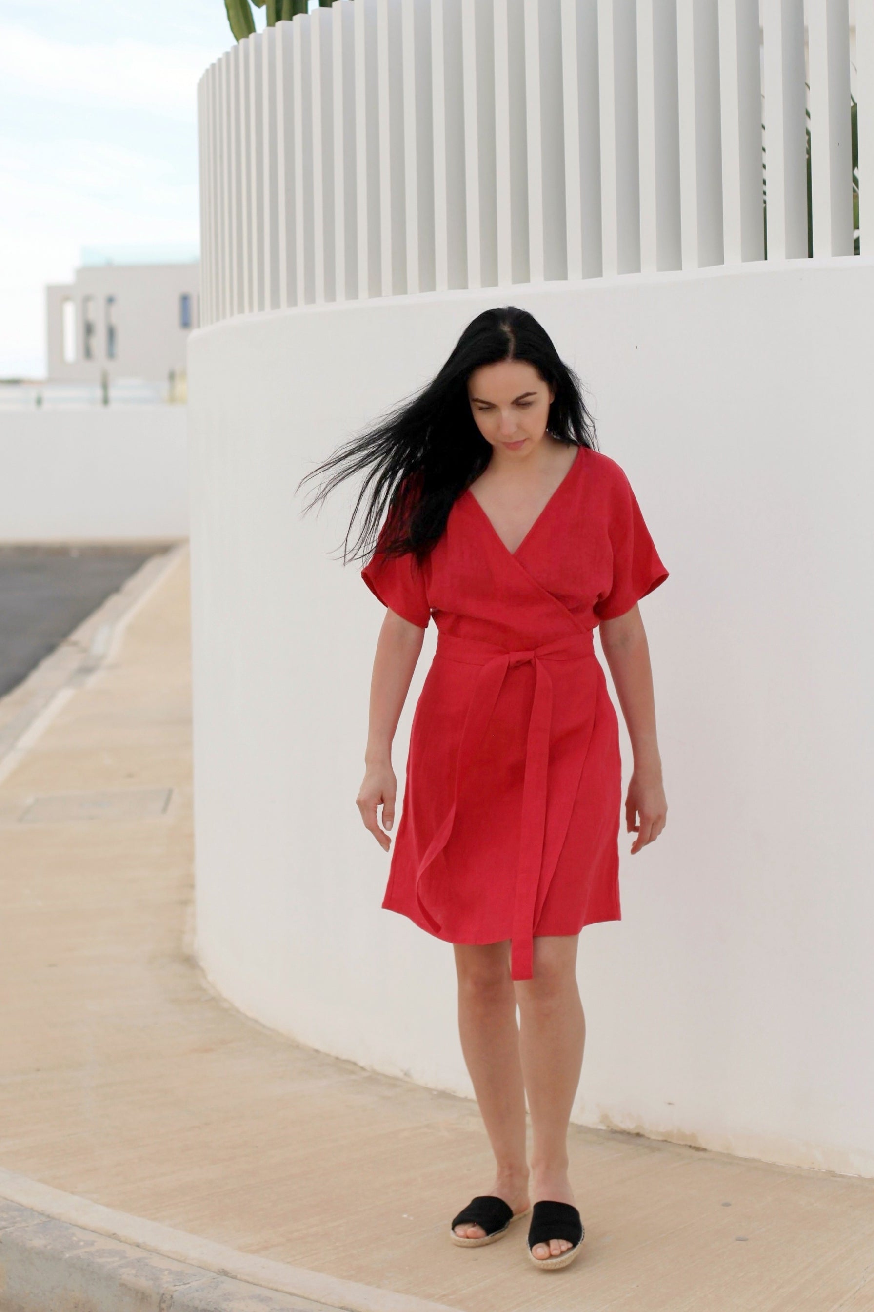 Woman in a red dress standing on a sidewalk with modern buildings in the background