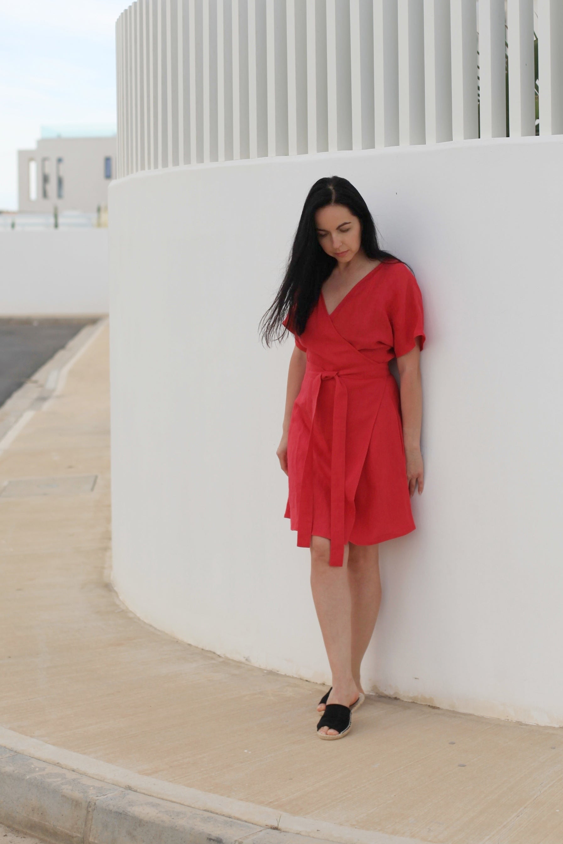 Woman in a red dress standing against a white wall outdoors