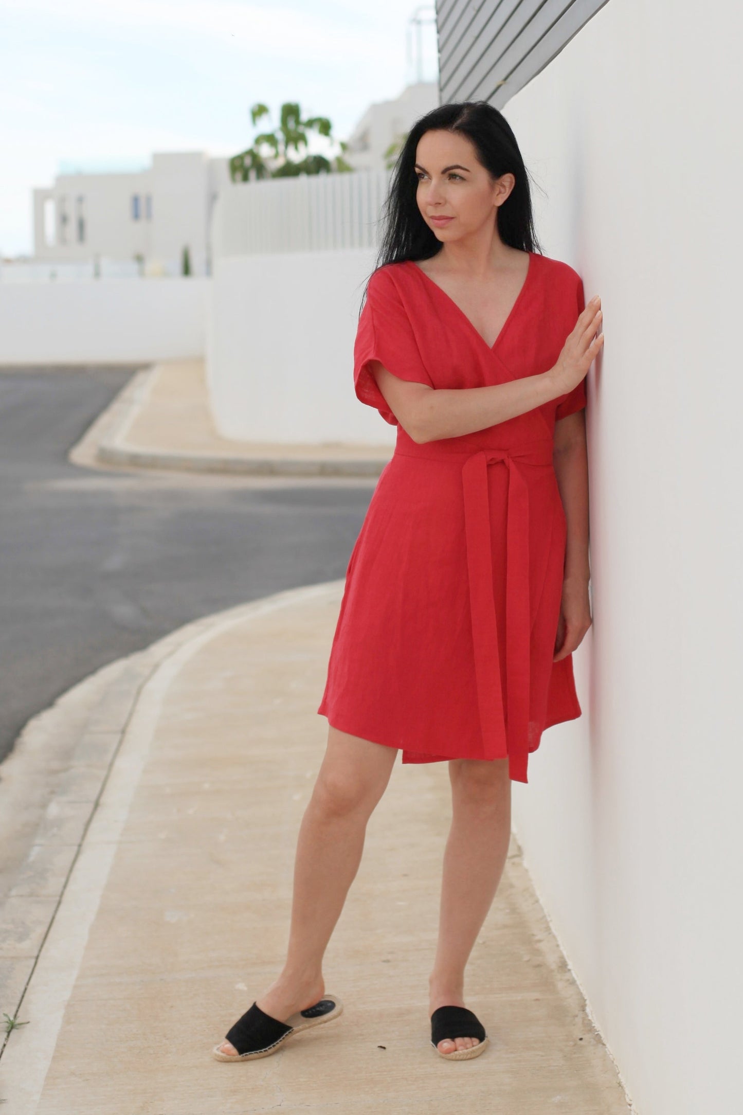 Woman in a red dress standing against a white wall on a street.