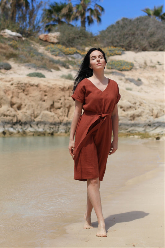 Woman in a rust-colored dress standing on a sandy beach with palm trees in the background