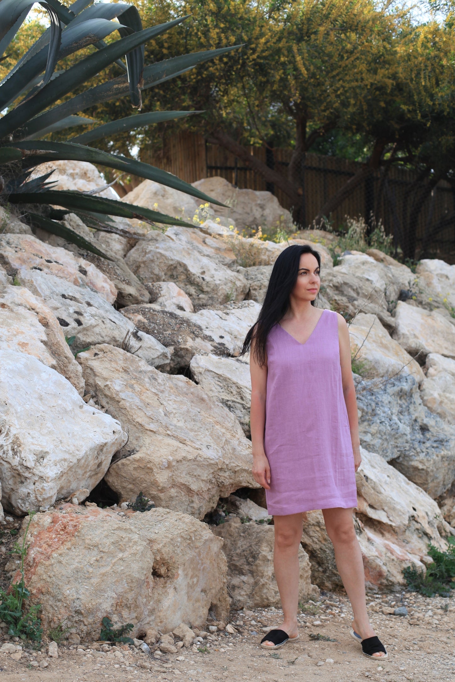 Woman in a purple dress standing among rocks with greenery in the background