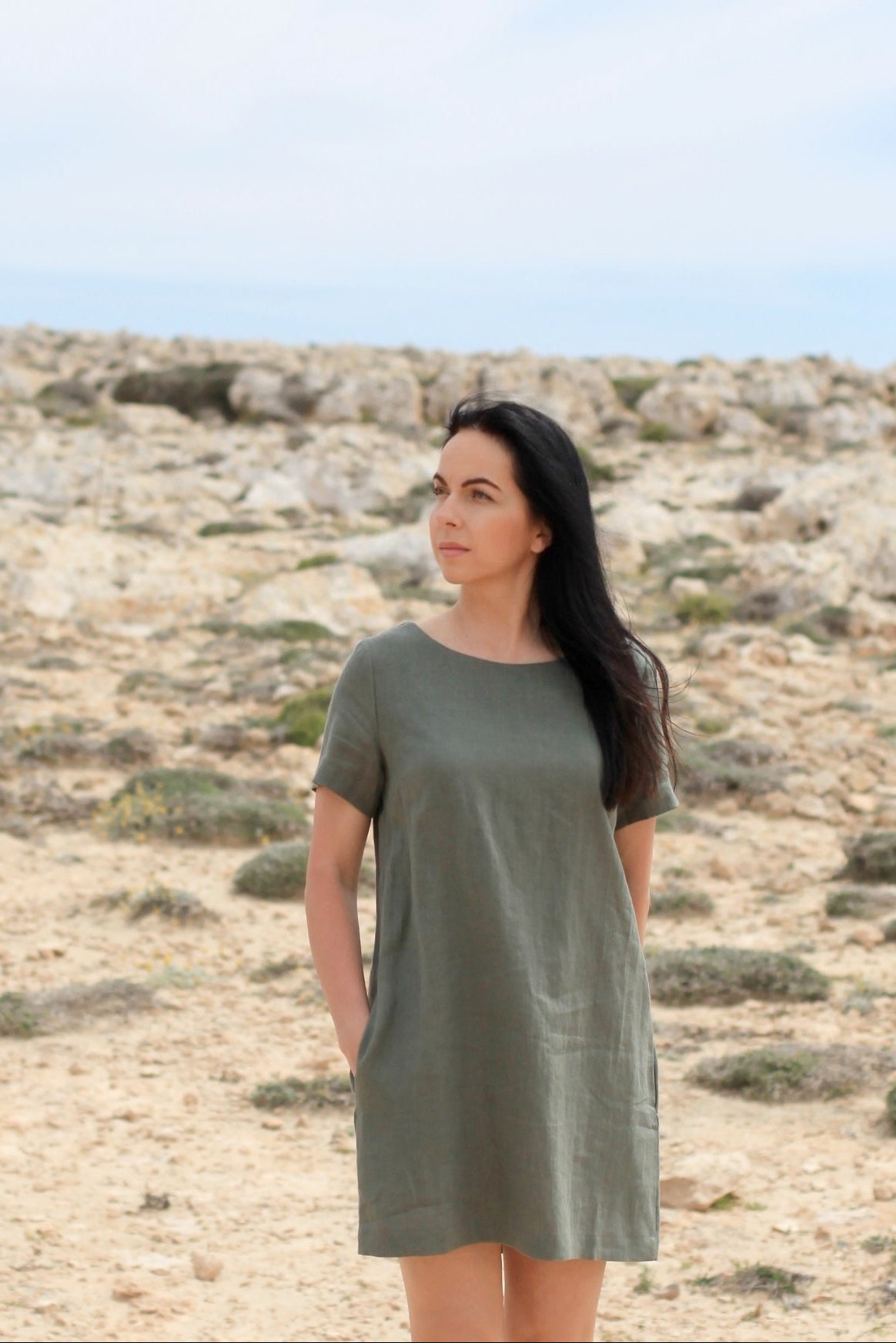 Woman in a green dress standing in a desert landscape with a clear blue sky.