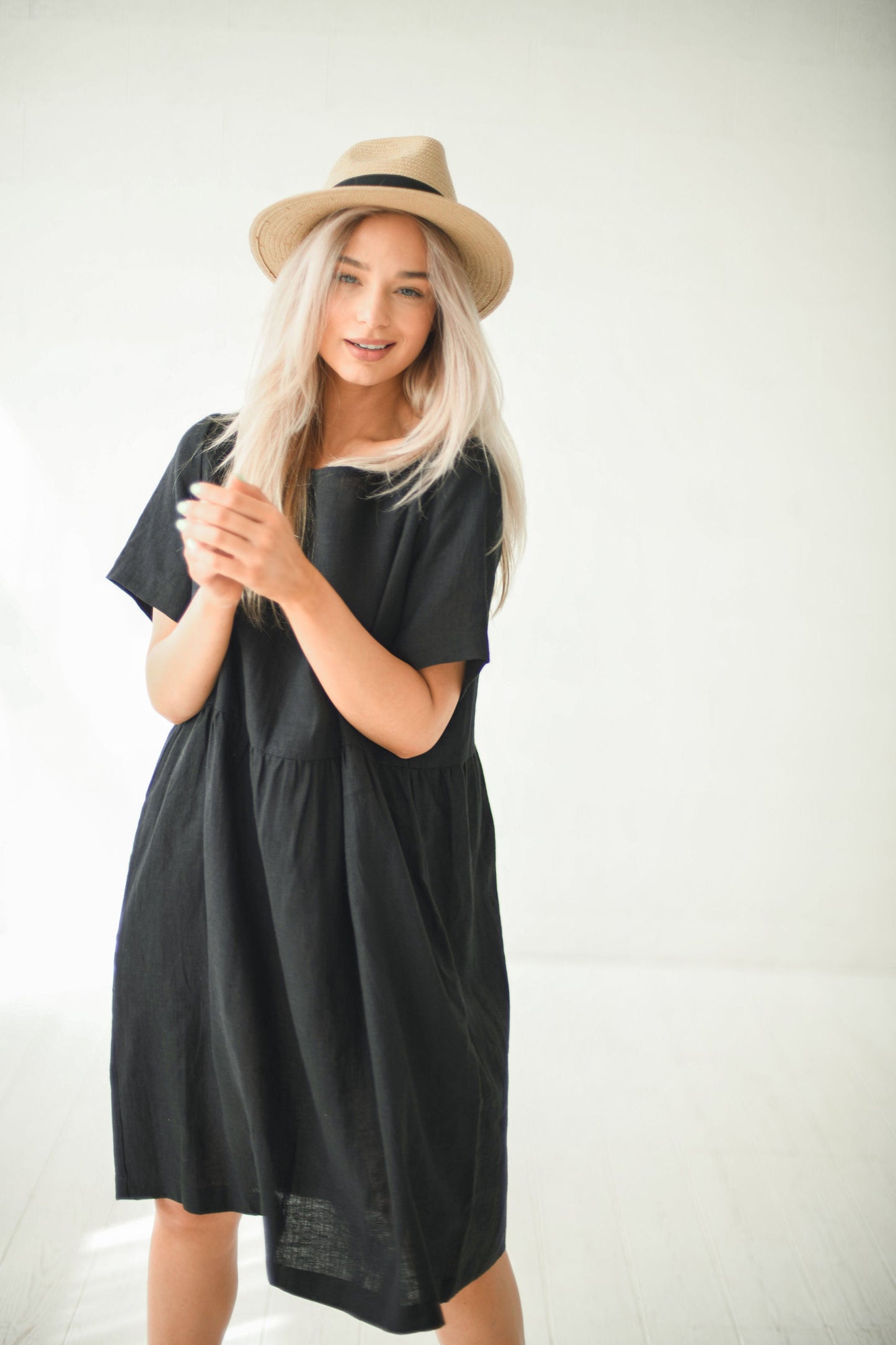 Alba black oversized linen dress seated with hat relaxed look holding hands handmade linen dress slow fashion