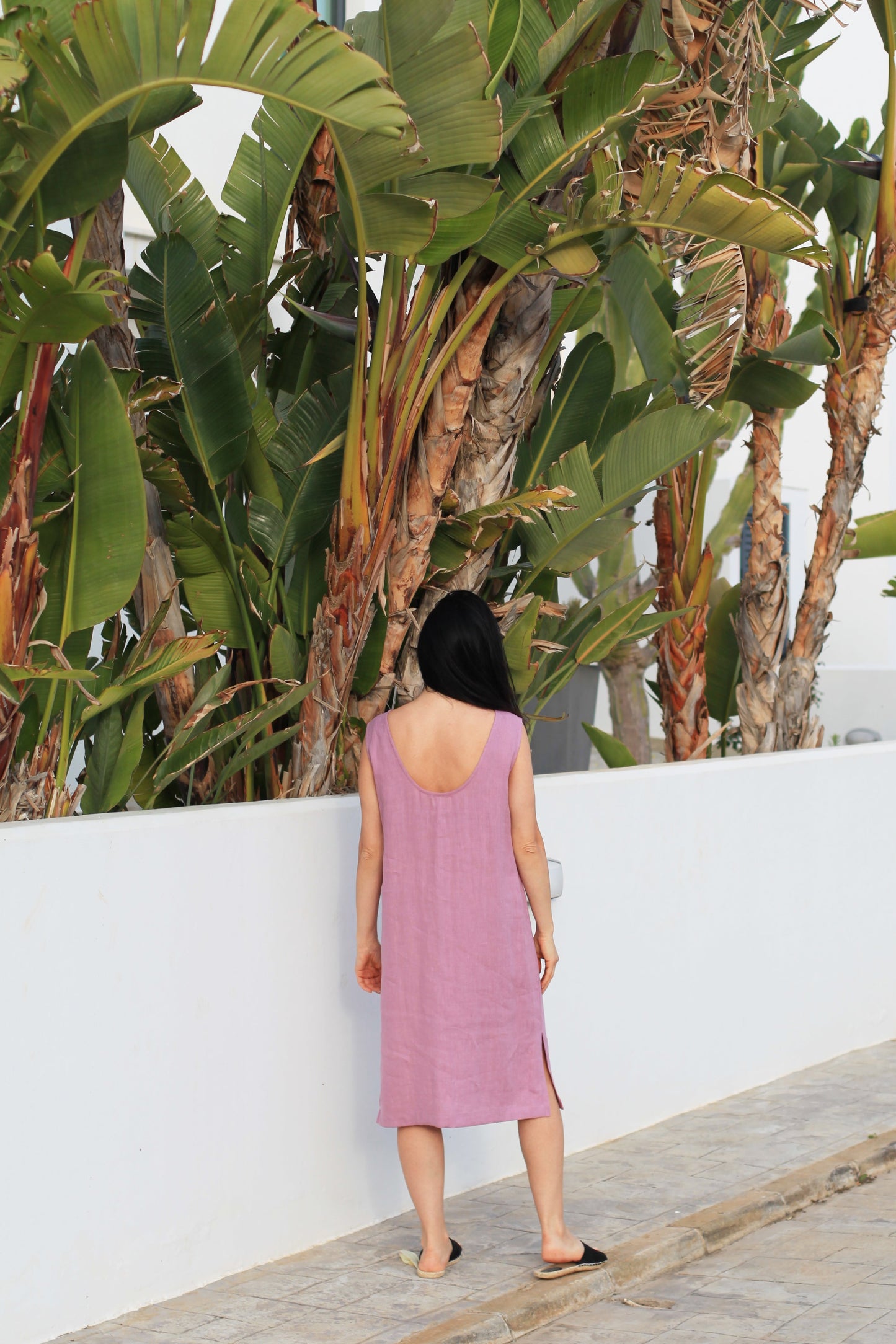 Woman in a pink dress walking along a path with tropical plants and a white wall in the background