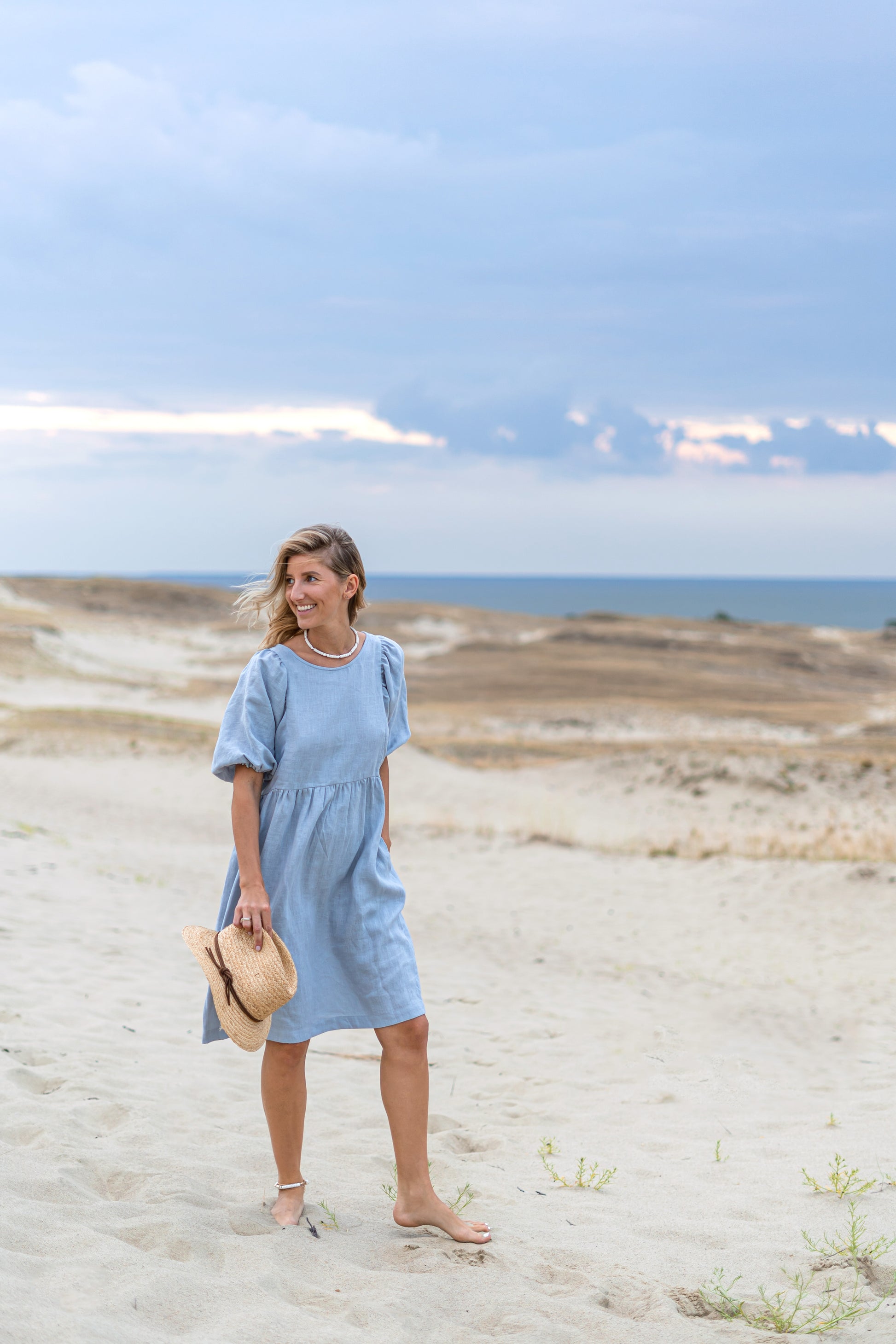 Light blue linen dress front-facing pose on beach showing minimalist design, handmade linen dress slow fashion
