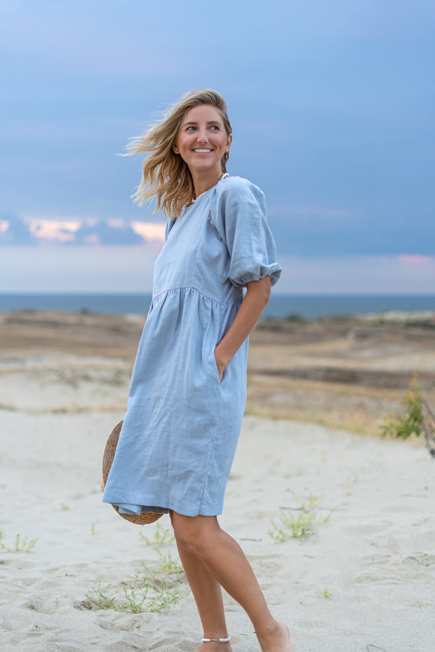 Light blue linen dress natural front view on beach showing relaxed silhouette, handmade linen dress slow fashion