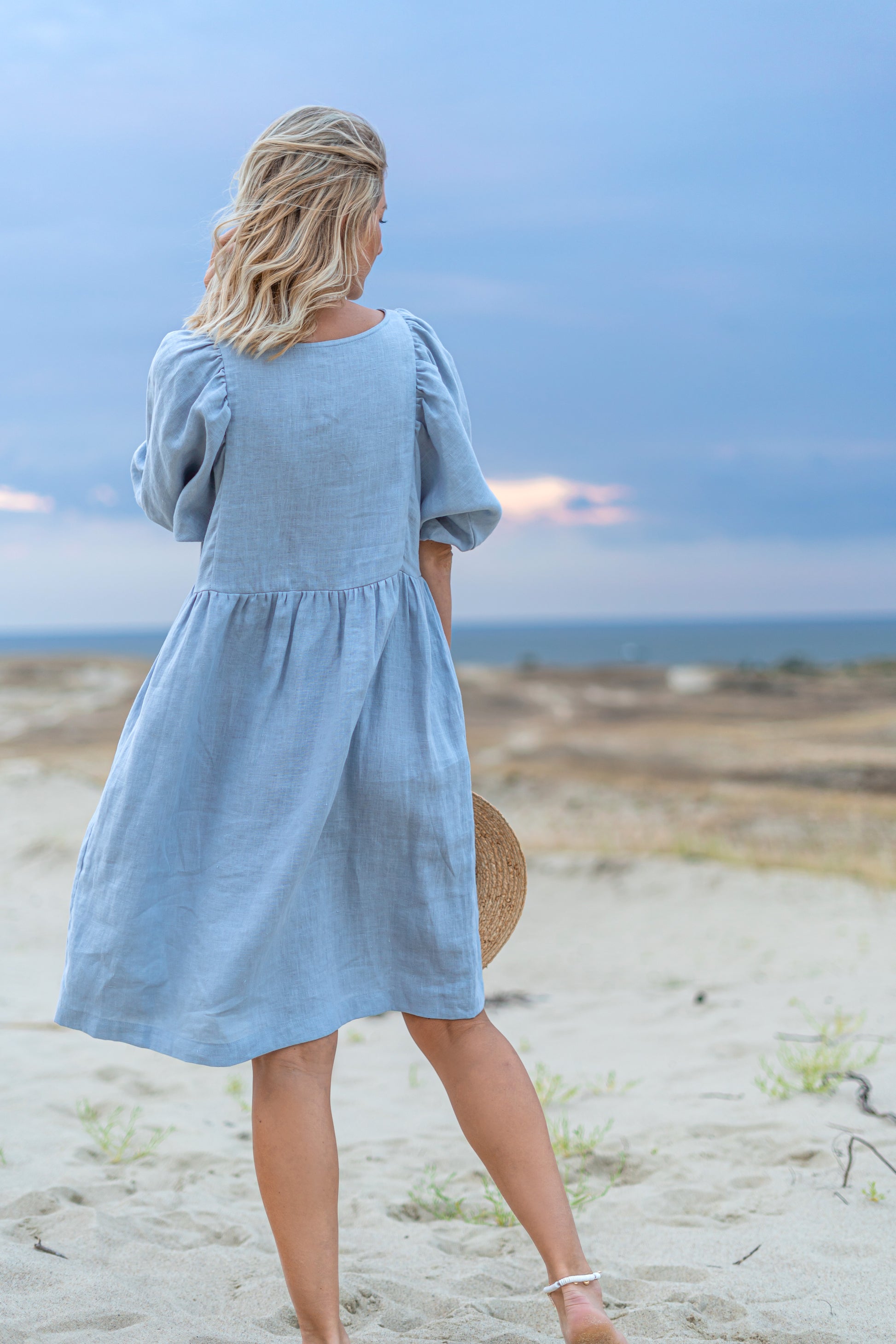 Light blue linen dress profile back view on beach showing knee-length cut, handmade linen dress slow fashion