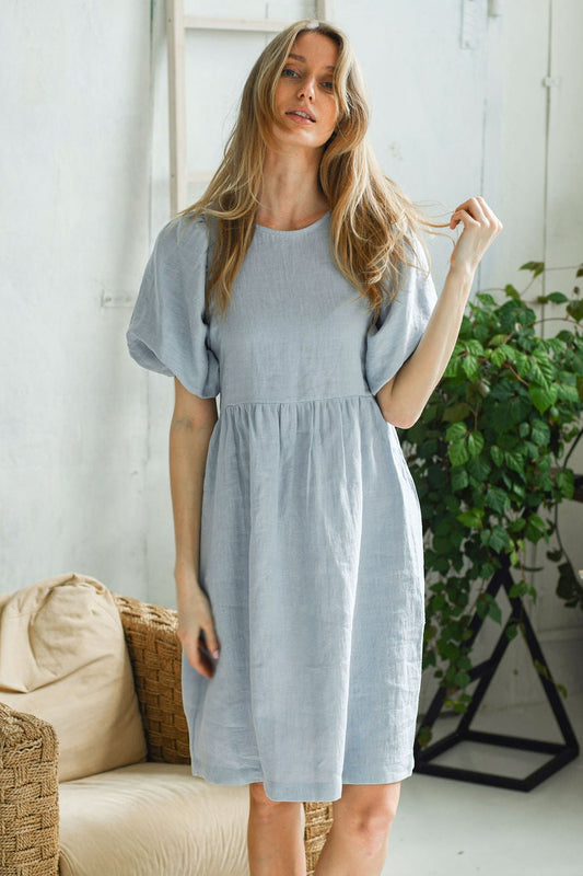 Dusty blue linen dress full-body pose with plants showing relaxed drape, handmade linen dress slow fashion