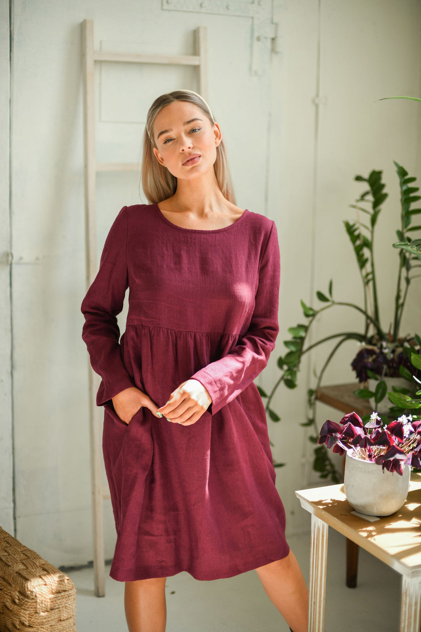 Dusty raspberry linen dress looking down softly with hands together showing relaxed fit, handmade linen dress slow fashion