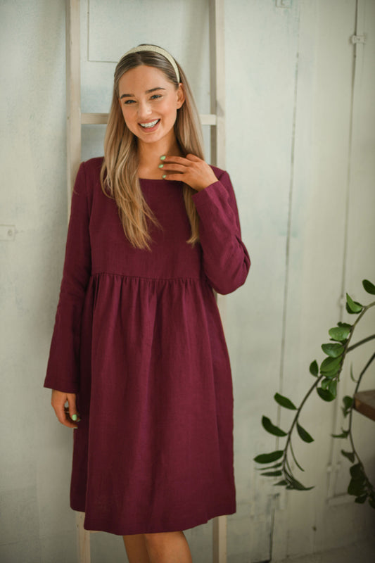 Dusty raspberry linen dress smiling gently in natural indoor setting showing minimalist design, handmade linen dress slow fashion