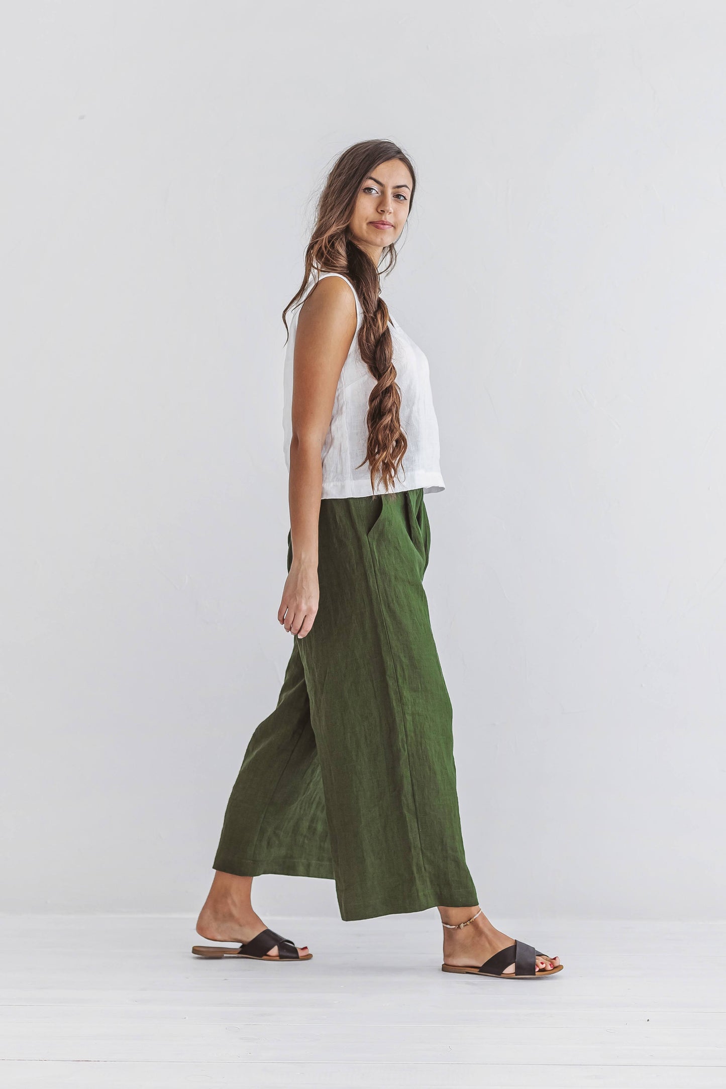 Forest green linen pants side walking pose showing soft natural drape and cropped length, handmade linen pants slow fashion