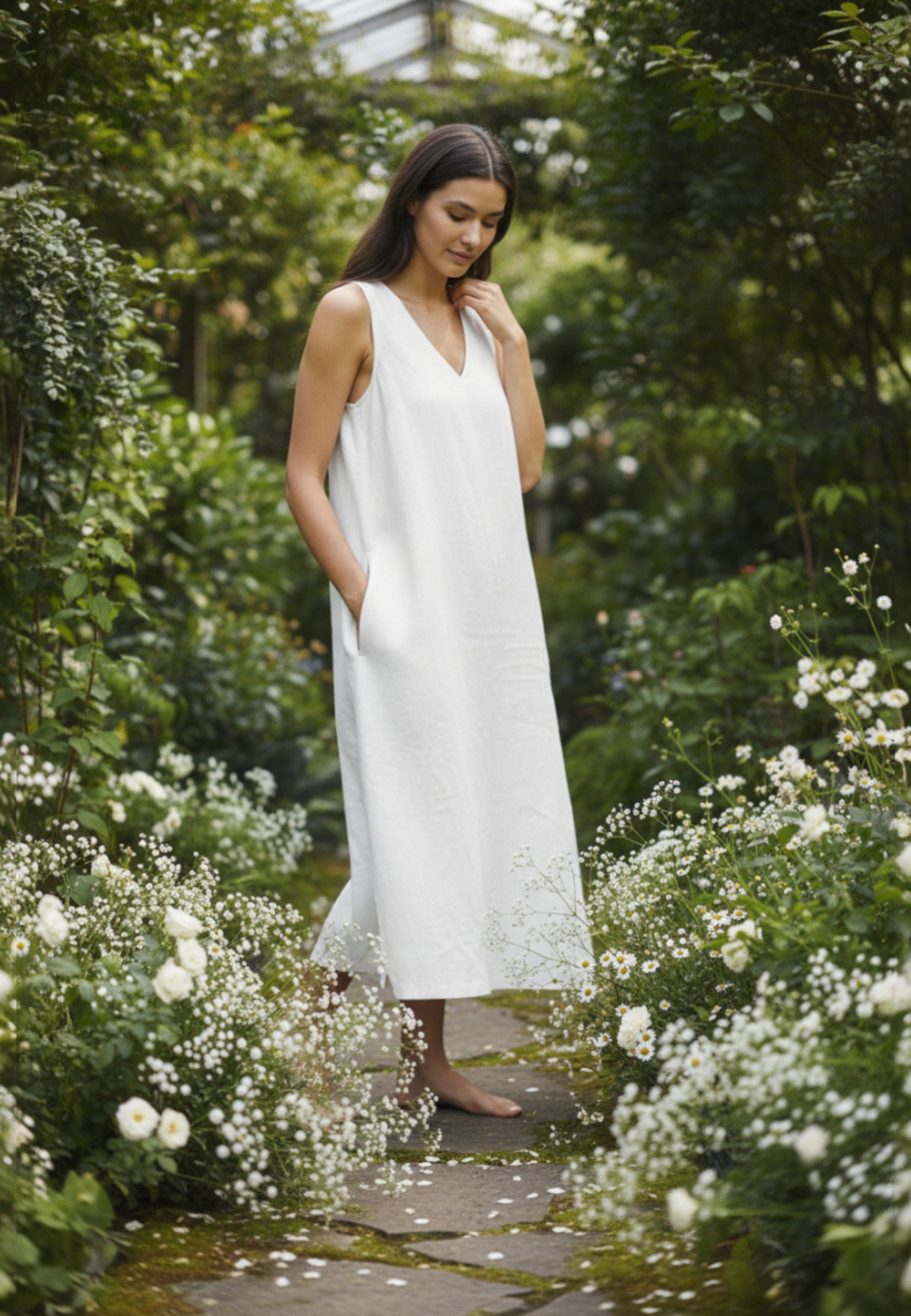 Woman in a white dress standing in a garden with greenery and flowers.