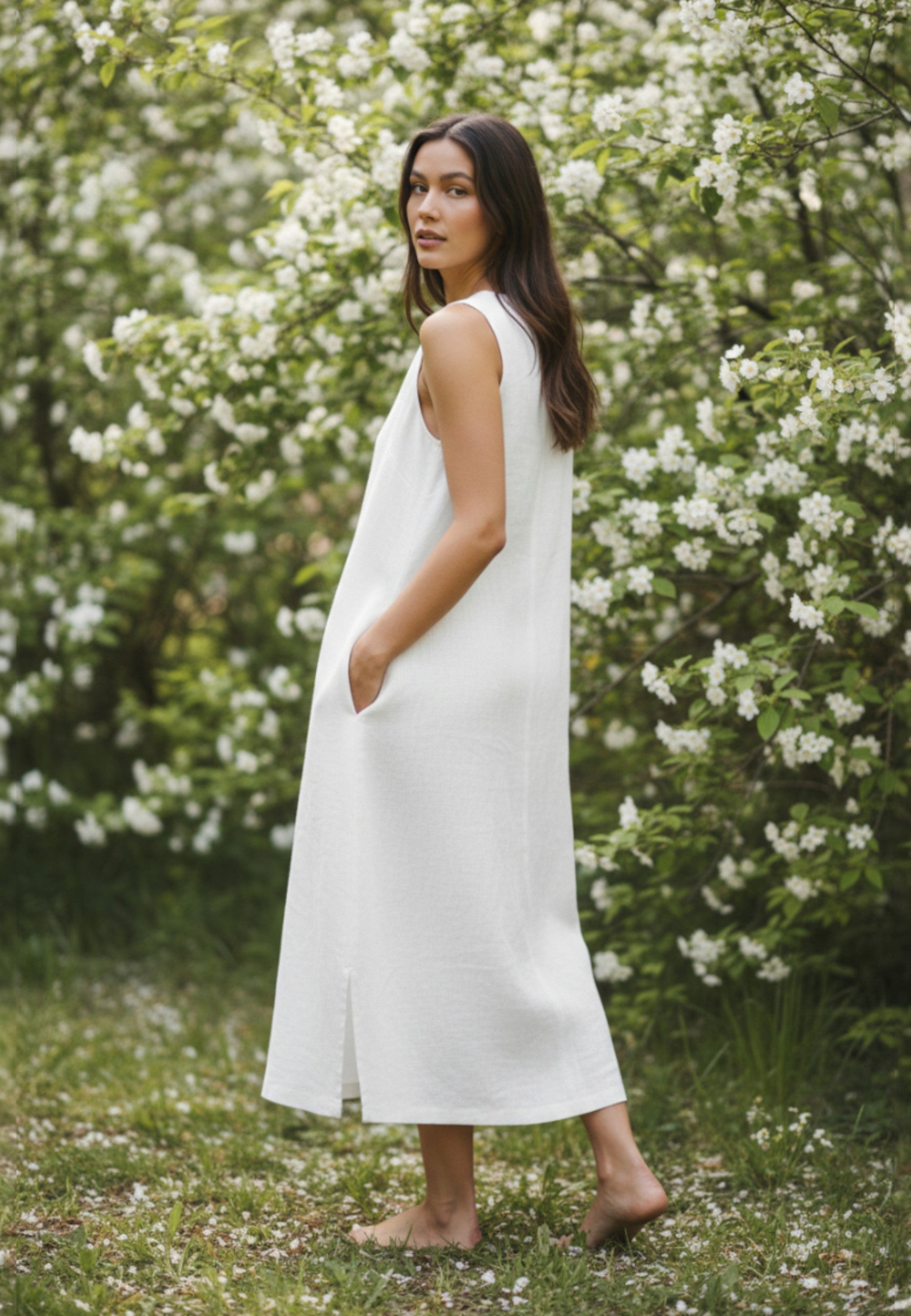Woman in a white dress standing in a garden with blooming trees.