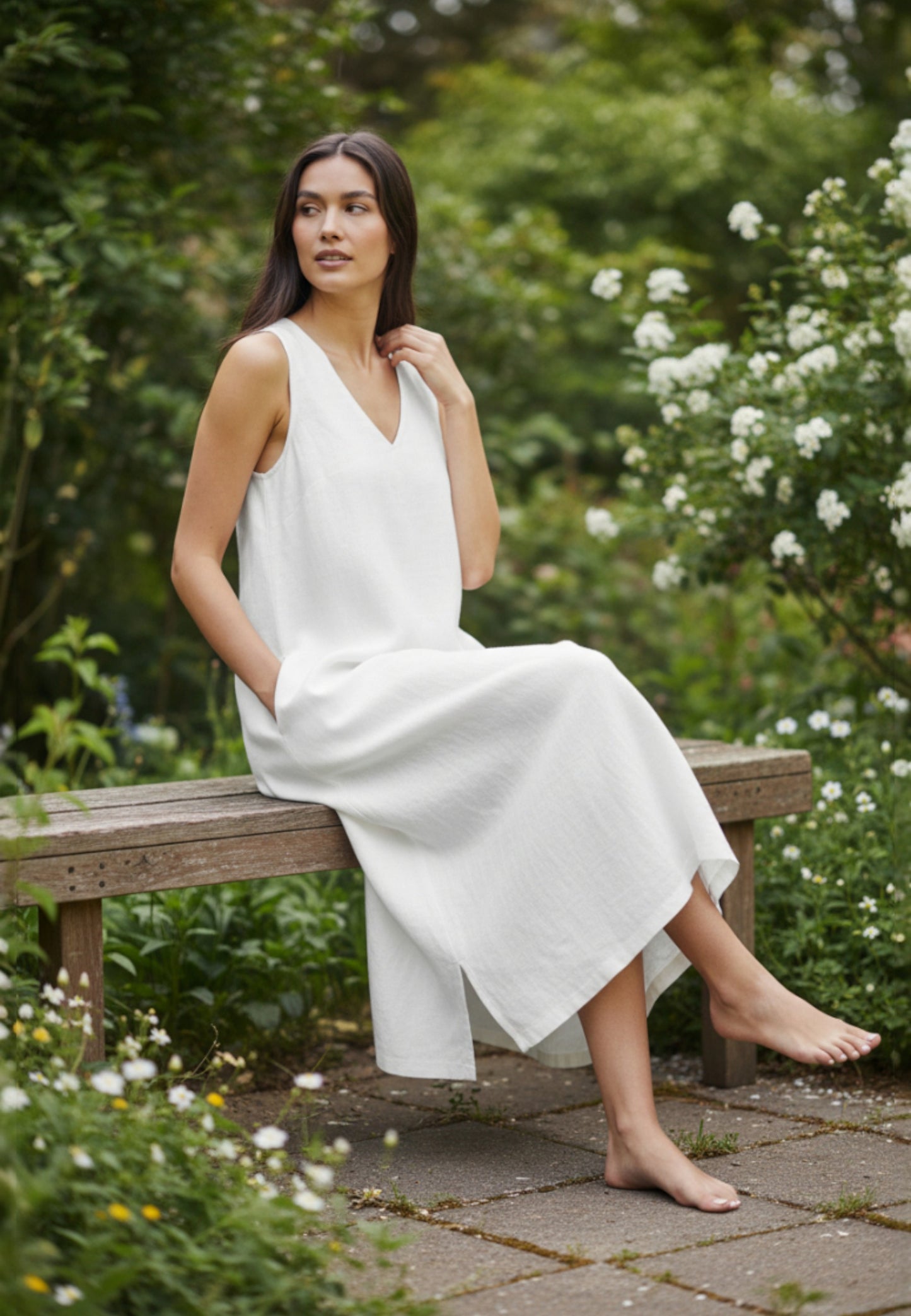 Woman in a white dress sitting on a wooden bench in a garden.