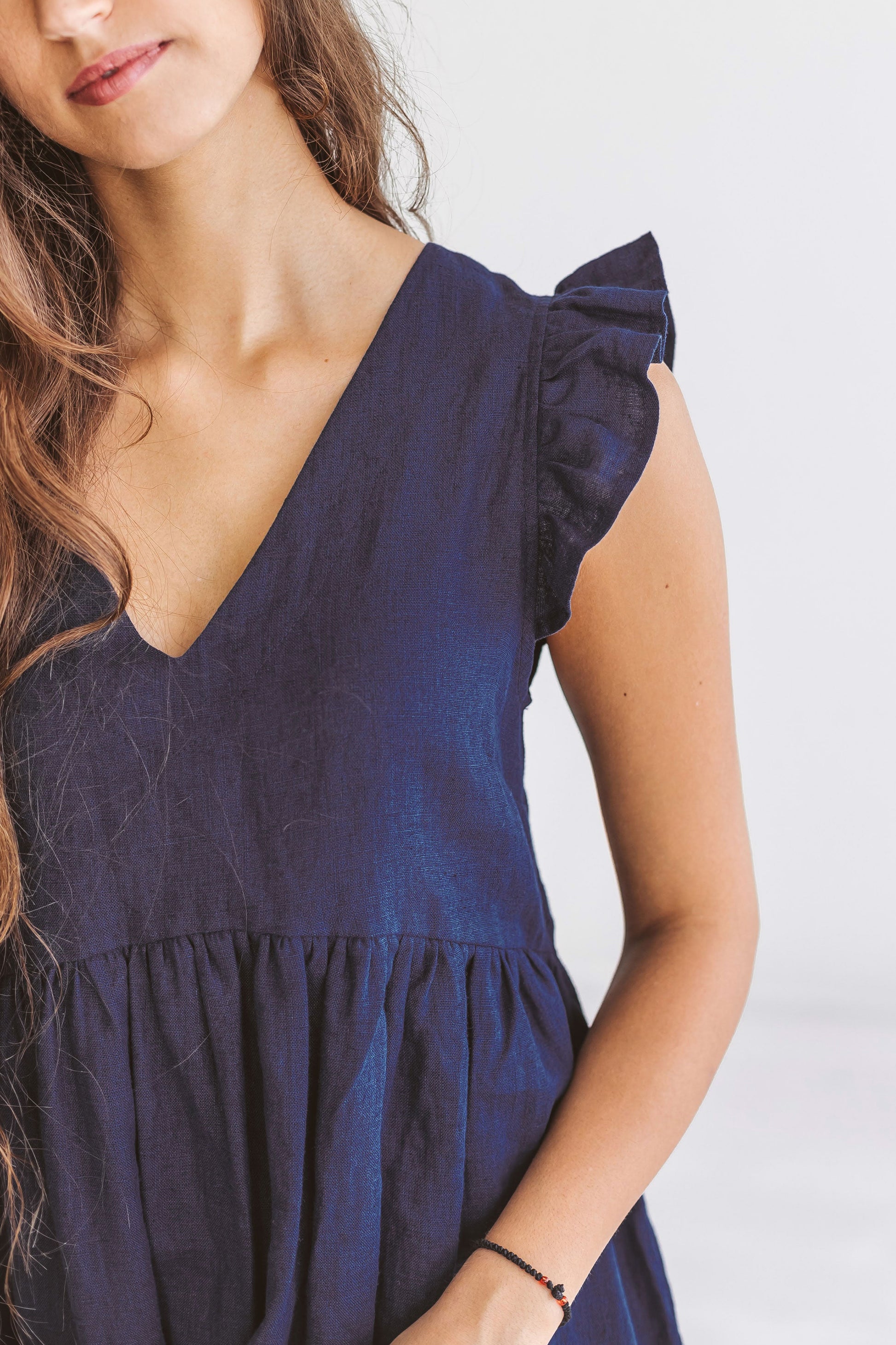 Close-up view of linen dress showing deep V-neckline and delicate gathered shoulder details.