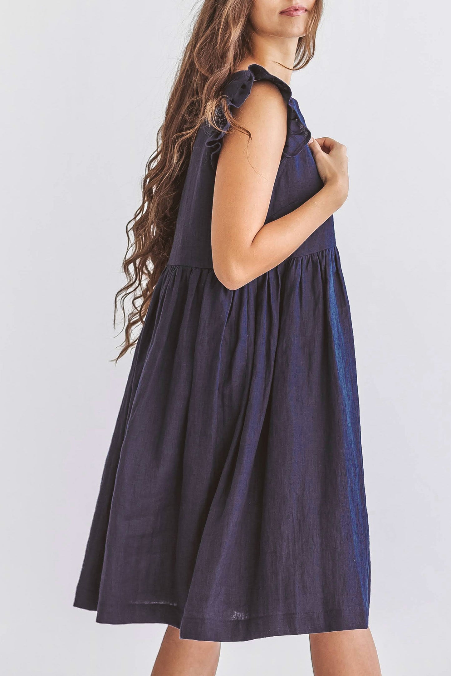 Side view of linen dress in natural light, showing airy drape and gentle shoulder details.