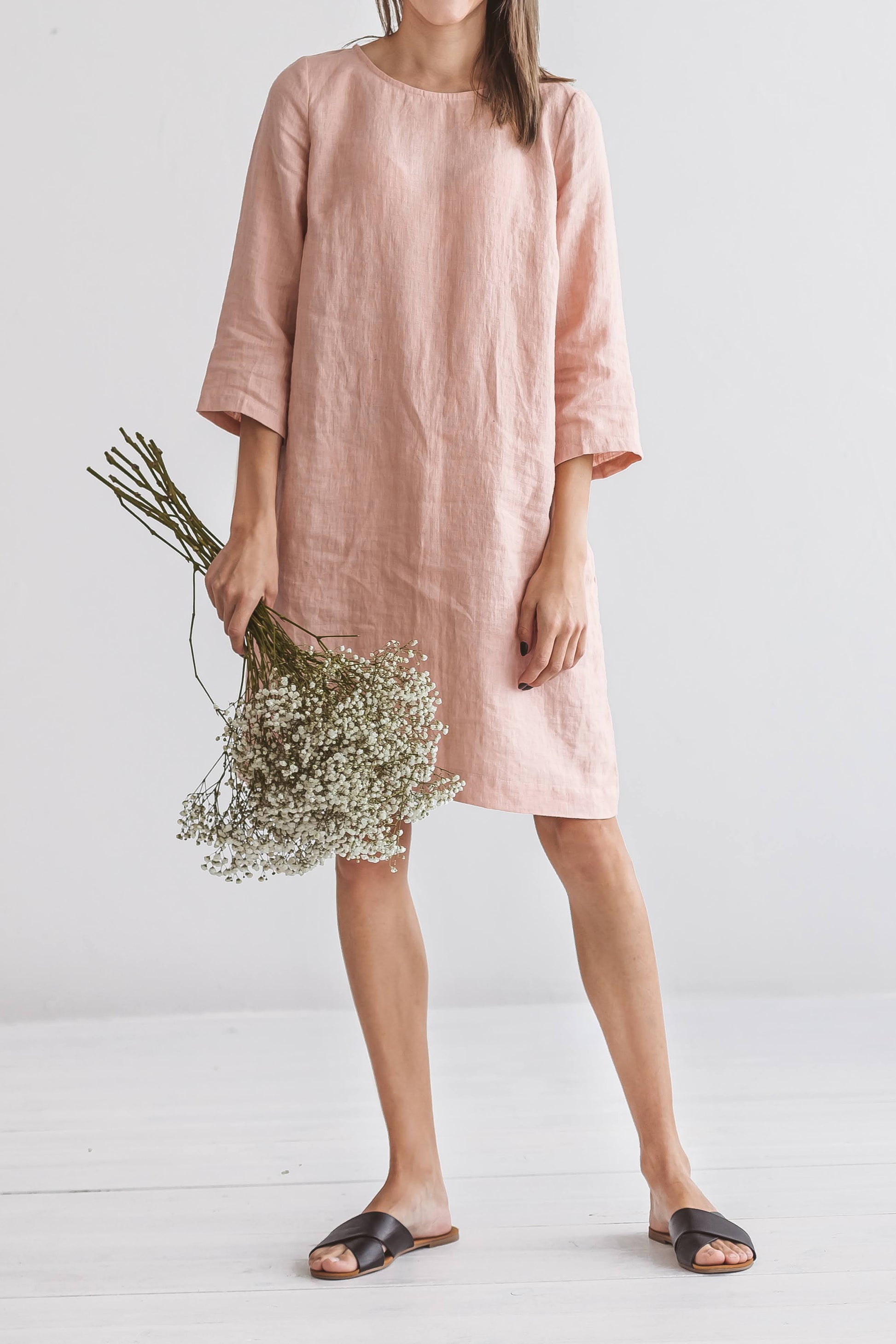 oman in Melinda linen dress, standing with flowers