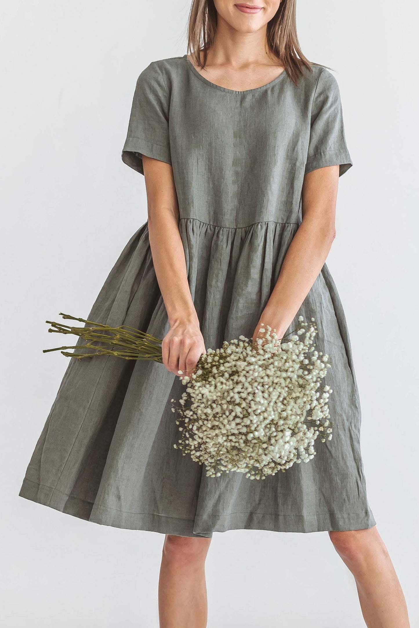 Khaki linen dress turning pose holding flowers showing skirt detail, handmade linen dress slow fashion