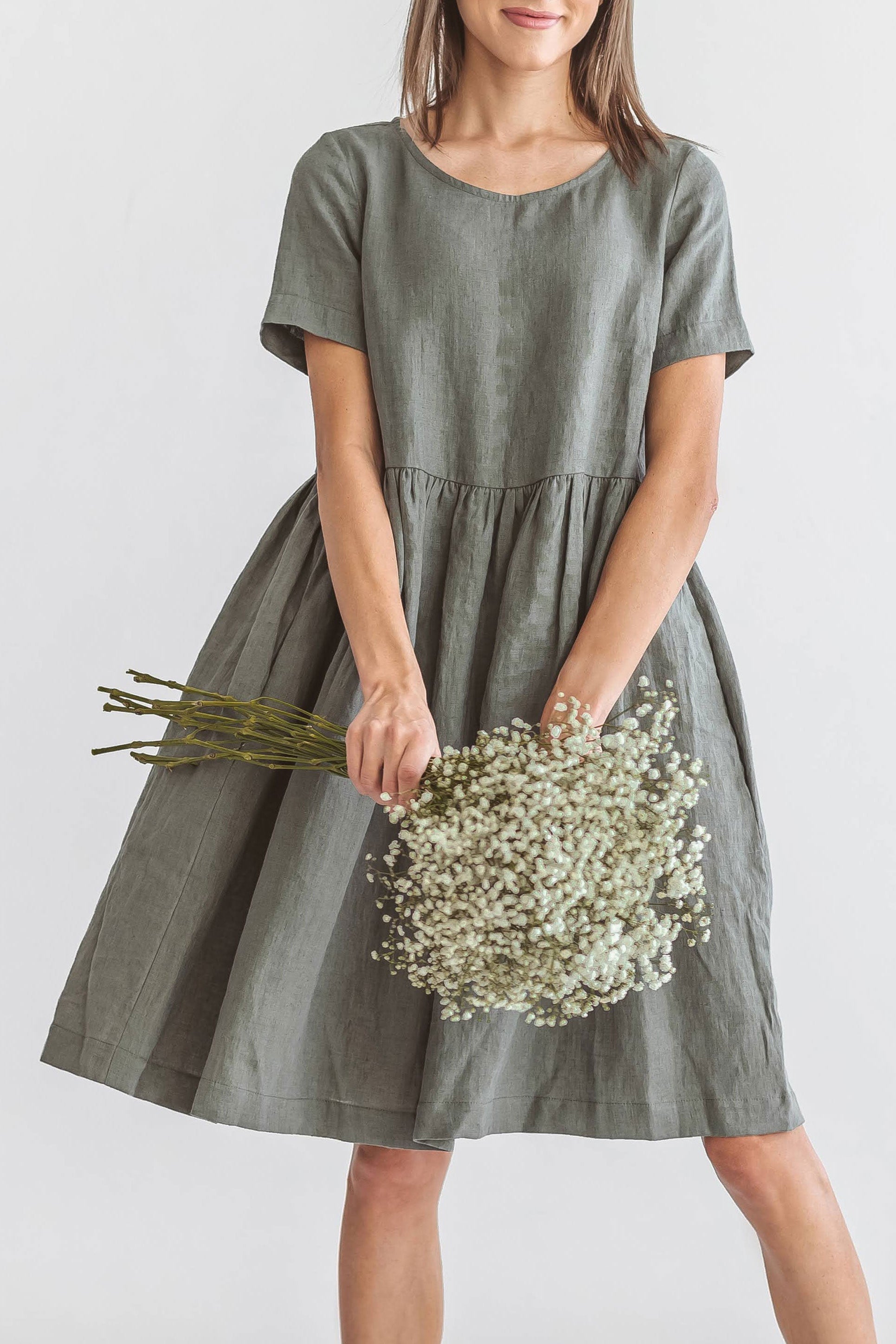 Khaki linen dress turning pose holding flowers showing skirt detail, handmade linen dress slow fashion
