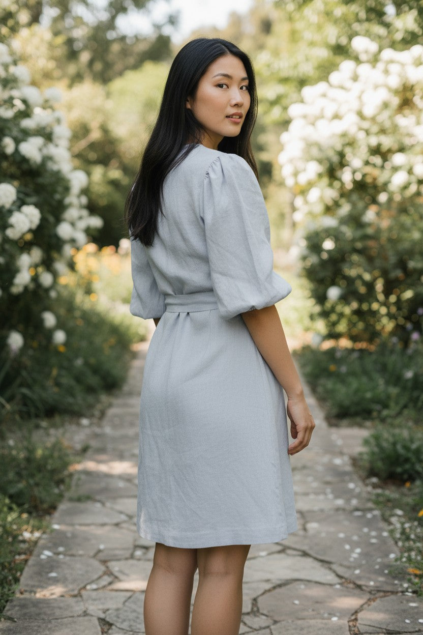 Woman in a light gray dress standing in a garden with white flowers and greenery.
