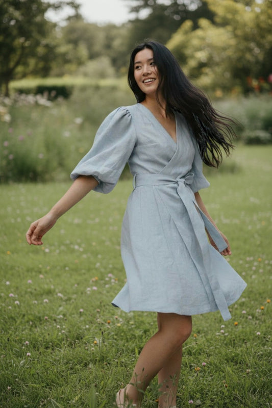 Woman in a light blue dress standing in a grassy field with trees in the background