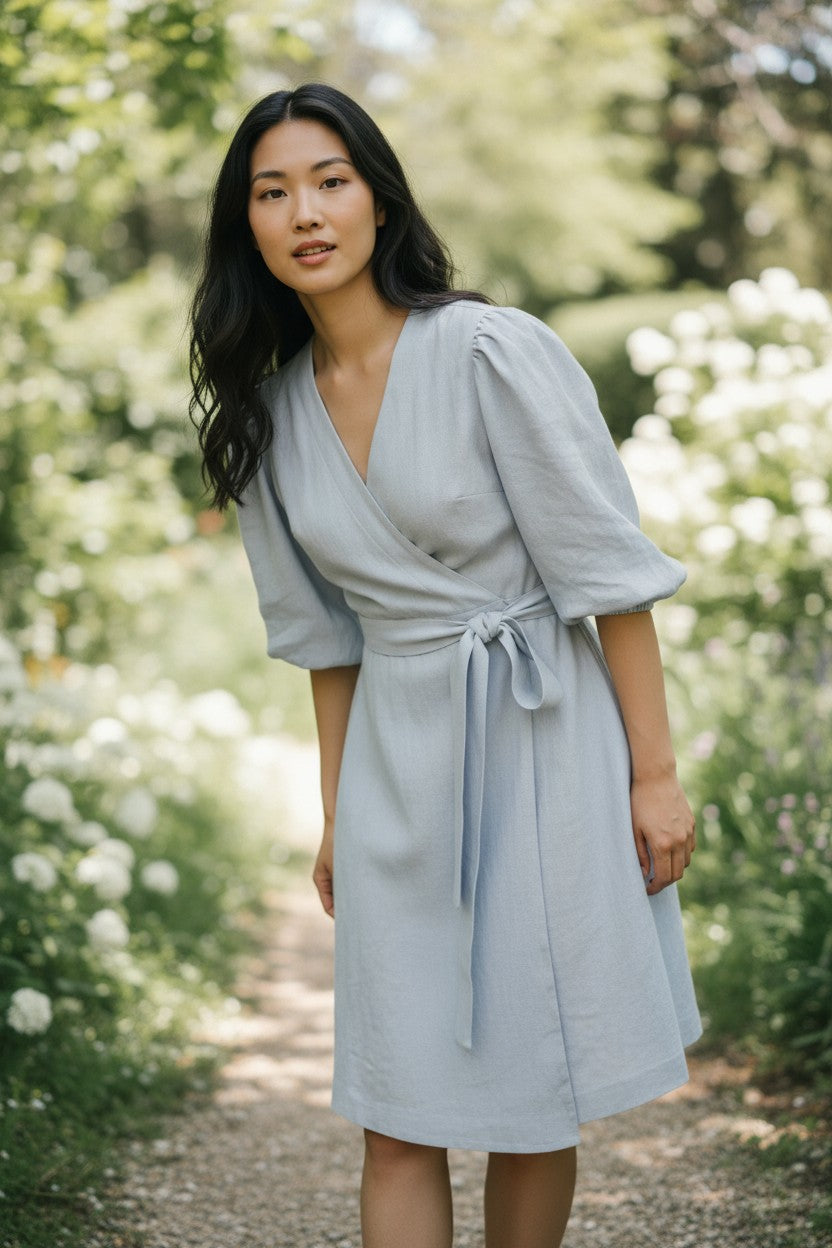 Woman in a light gray dress standing in a garden with greenery and flowers.