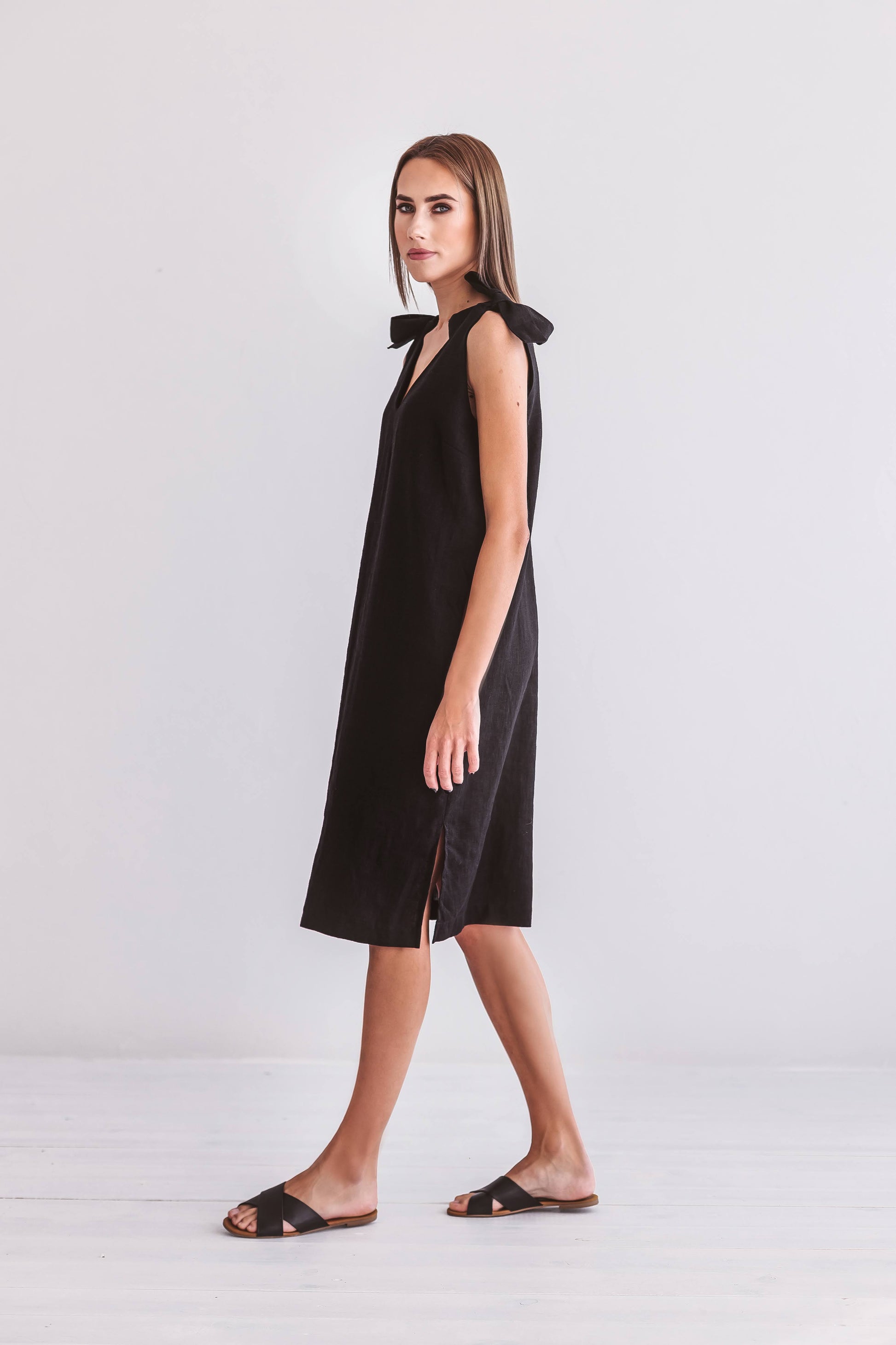 Black linen dress in natural light standing sideways showing sleeveless cut, handmade linen dress slow fashion
