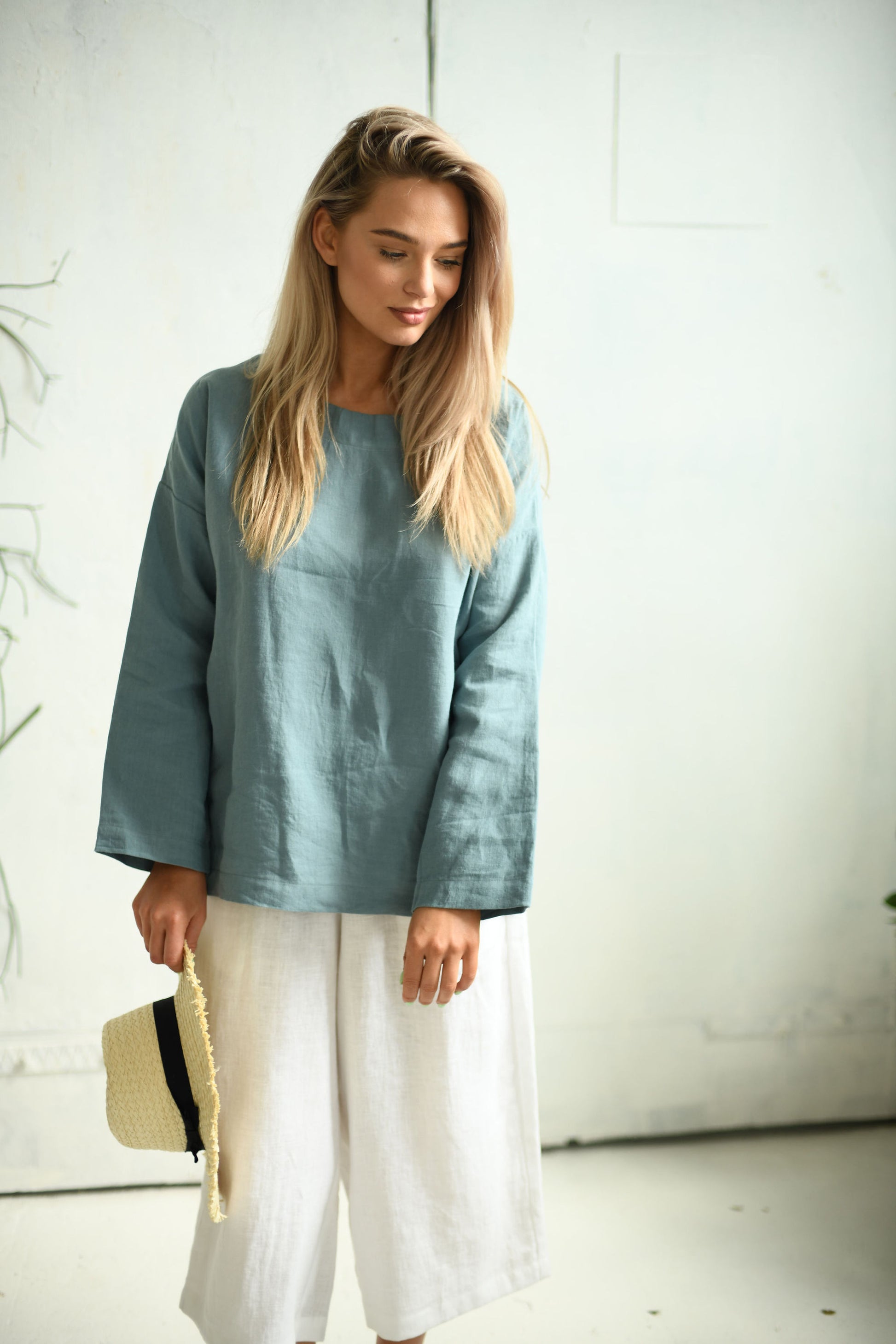 White linen pants relaxed front view holding hat showing wide-leg silhouette, handmade linen pants slow fashion