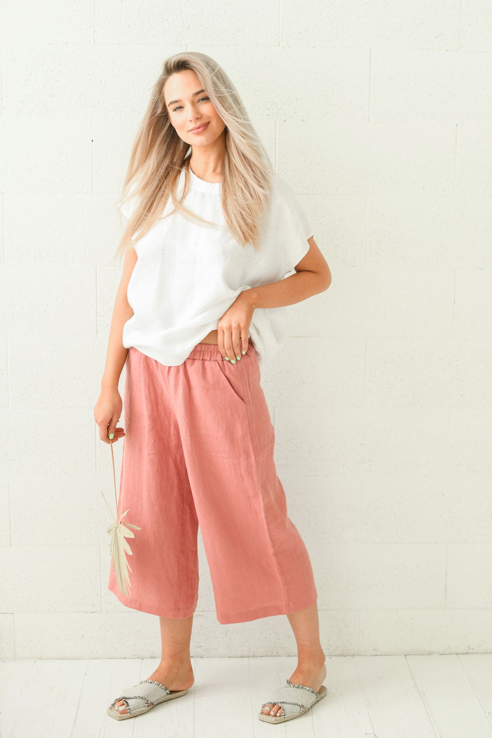 Salmon linen pants holding dried palm leaf smiling showing relaxed styling, handmade linen pants slow fashion