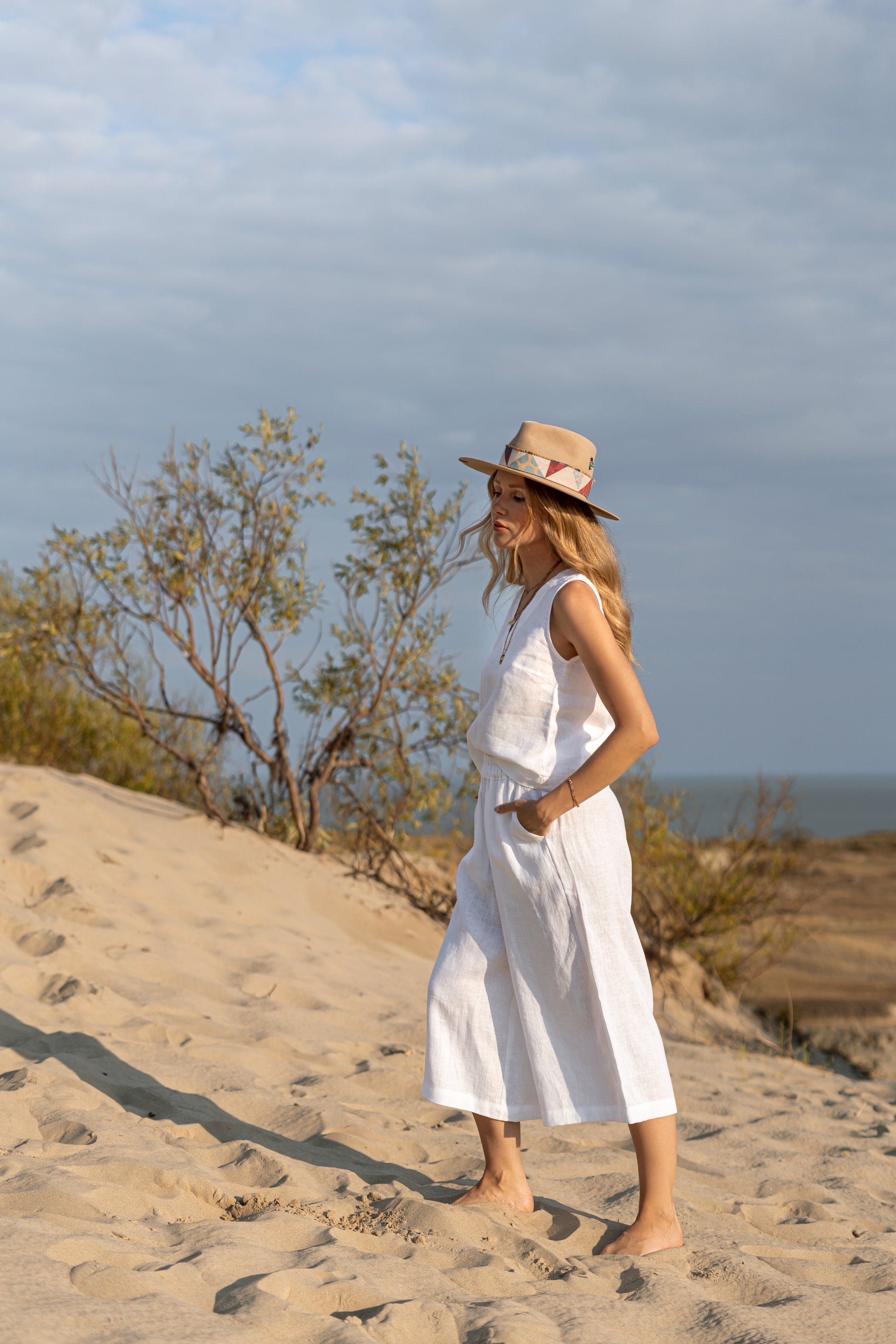 White linen pants standing on sand in calm outdoor setting showing wide-leg cut, handmade linen pants slow fashion