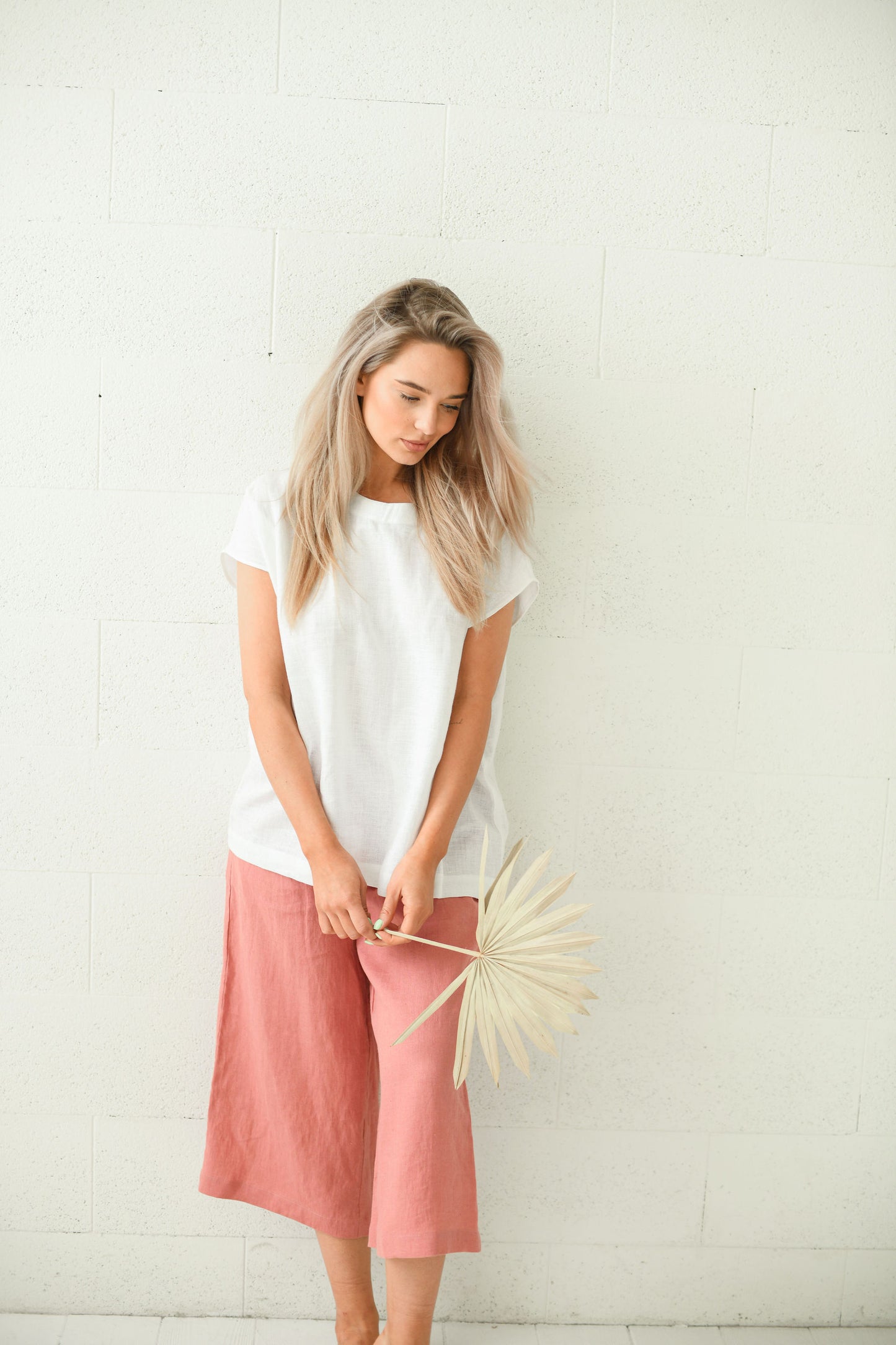 Salmon linen pants looking down in gentle turning pose showing relaxed drape, handmade linen pants slow fashion