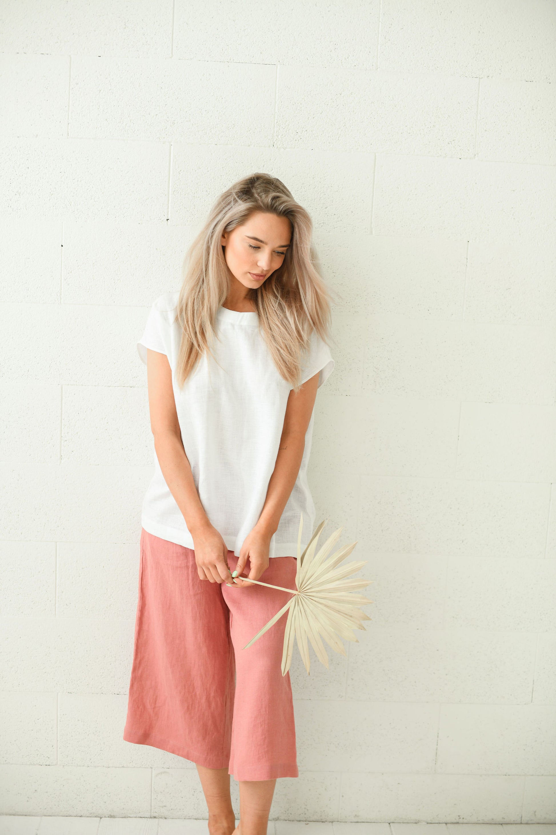 Salmon linen pants looking down in gentle turning pose showing relaxed drape, handmade linen pants slow fashion