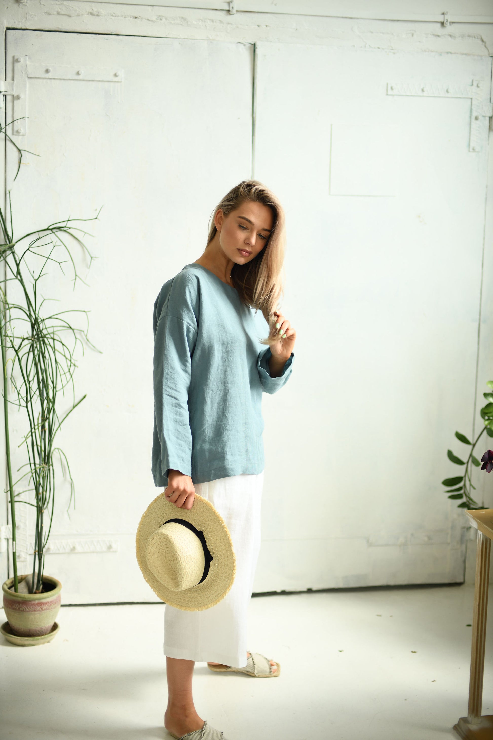 White linen pants standing in soft natural indoor light showing wide-leg cut, handmade linen pants slow fashion